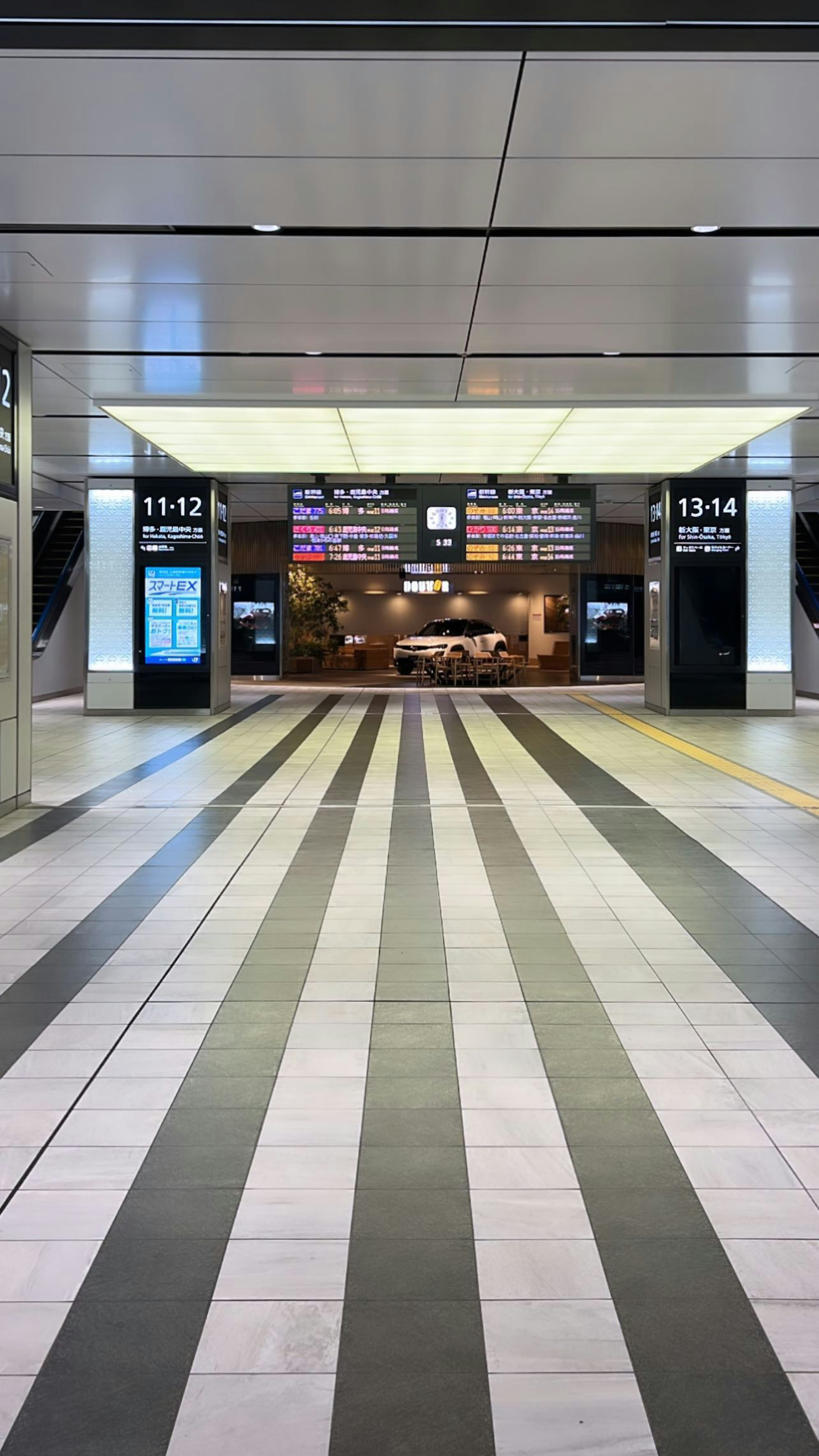 Interno di una stazione ferroviaria con pavimento a strisce e segnaletica digitale