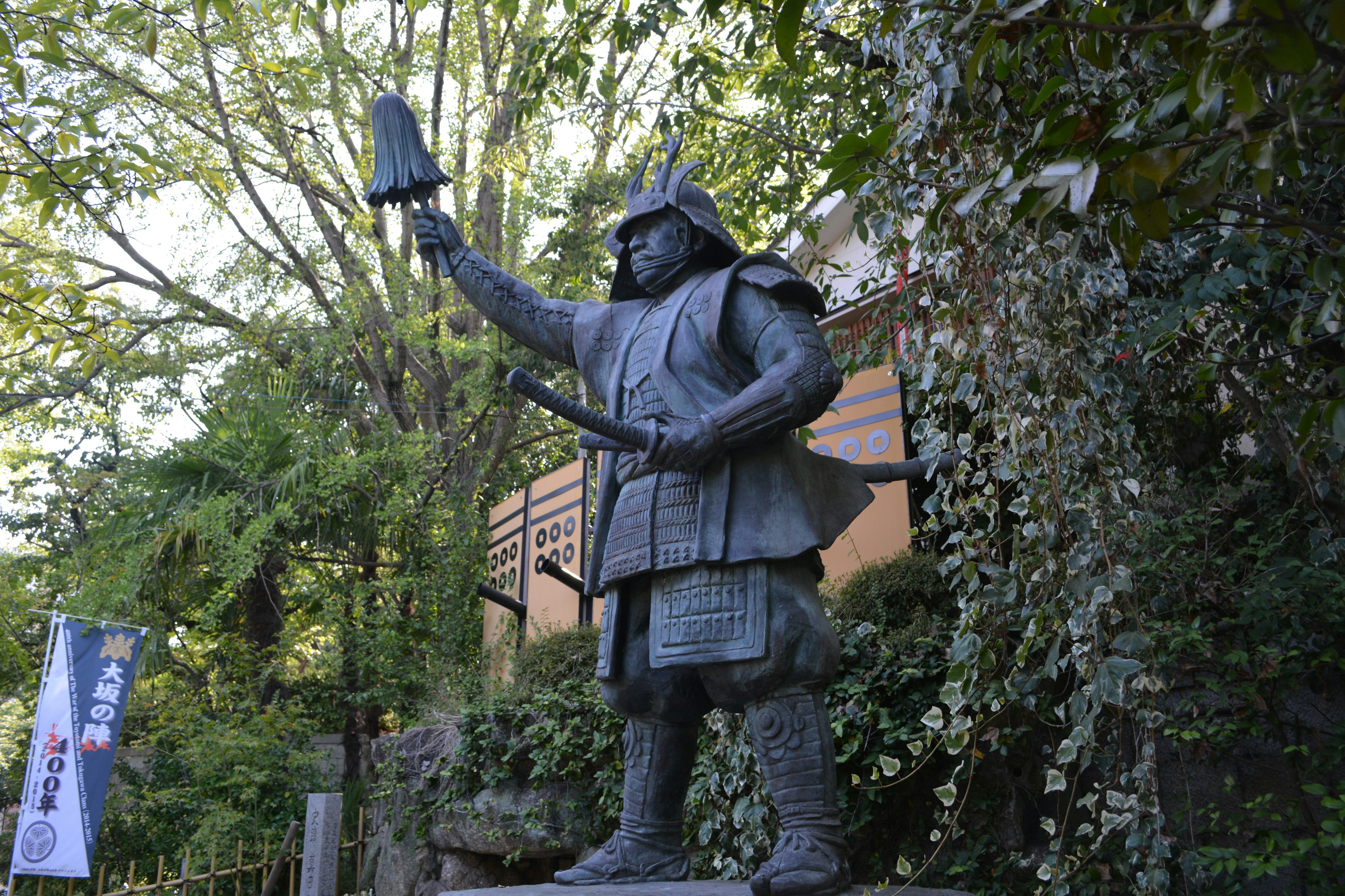 A samurai statue holding a bell surrounded by lush greenery