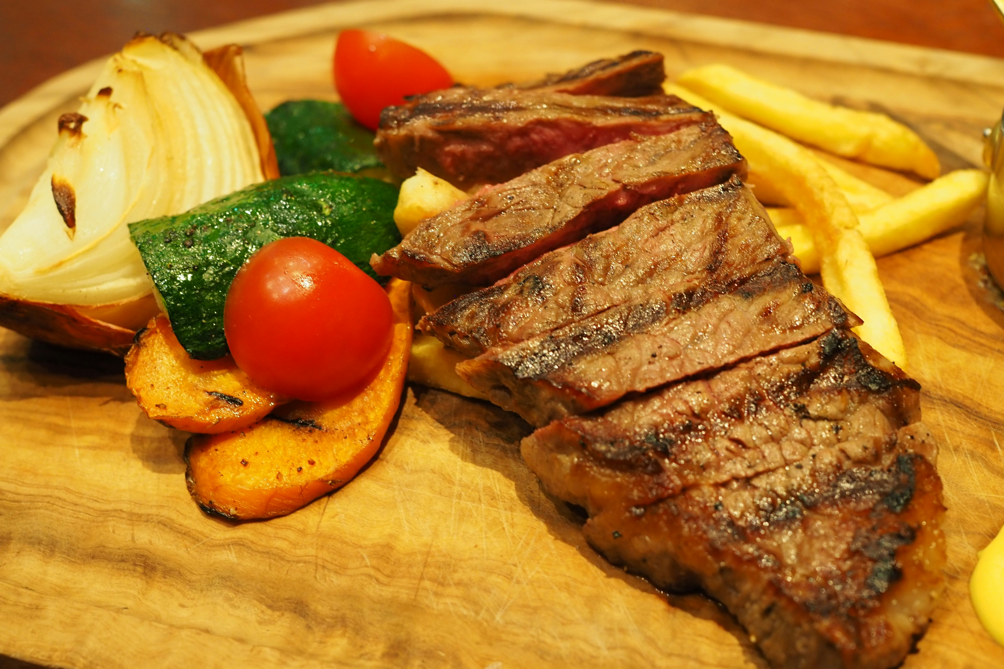 In Scheiben geschnittenes Steak auf einem Holzbrett serviert mit buntem Gemüse und Pommes Frites