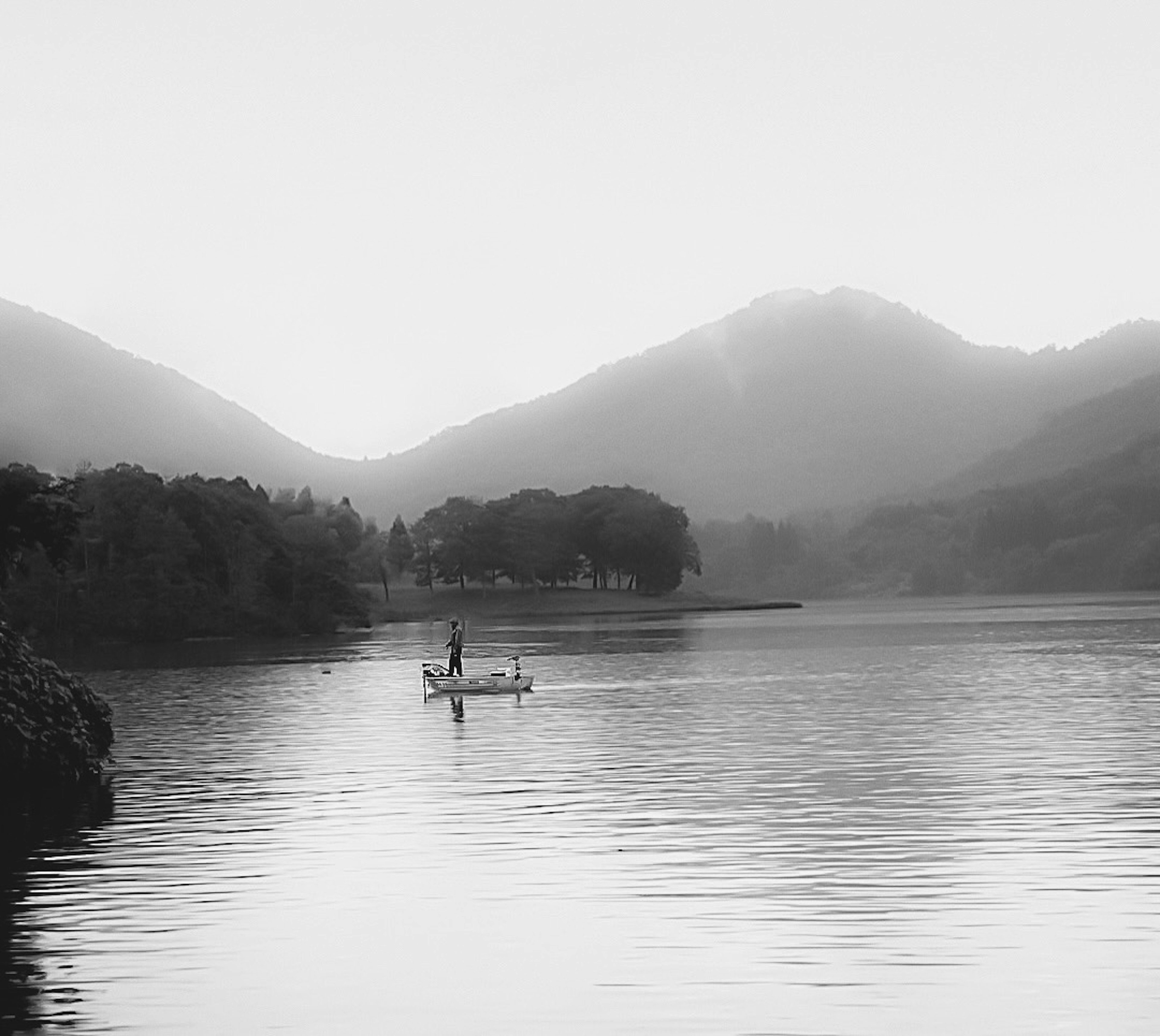 A small boat floats on a calm lake surrounded by misty mountains