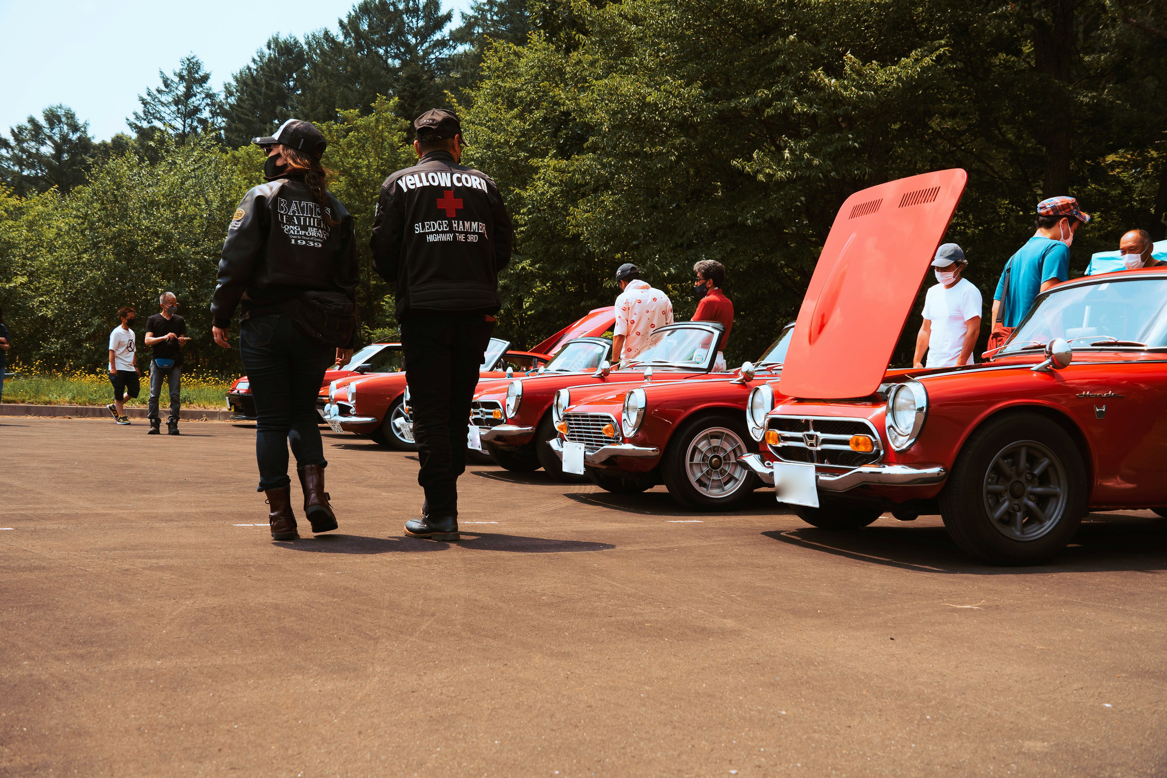 Auto classiche rosse in fila a un evento con partecipanti che osservano i veicoli