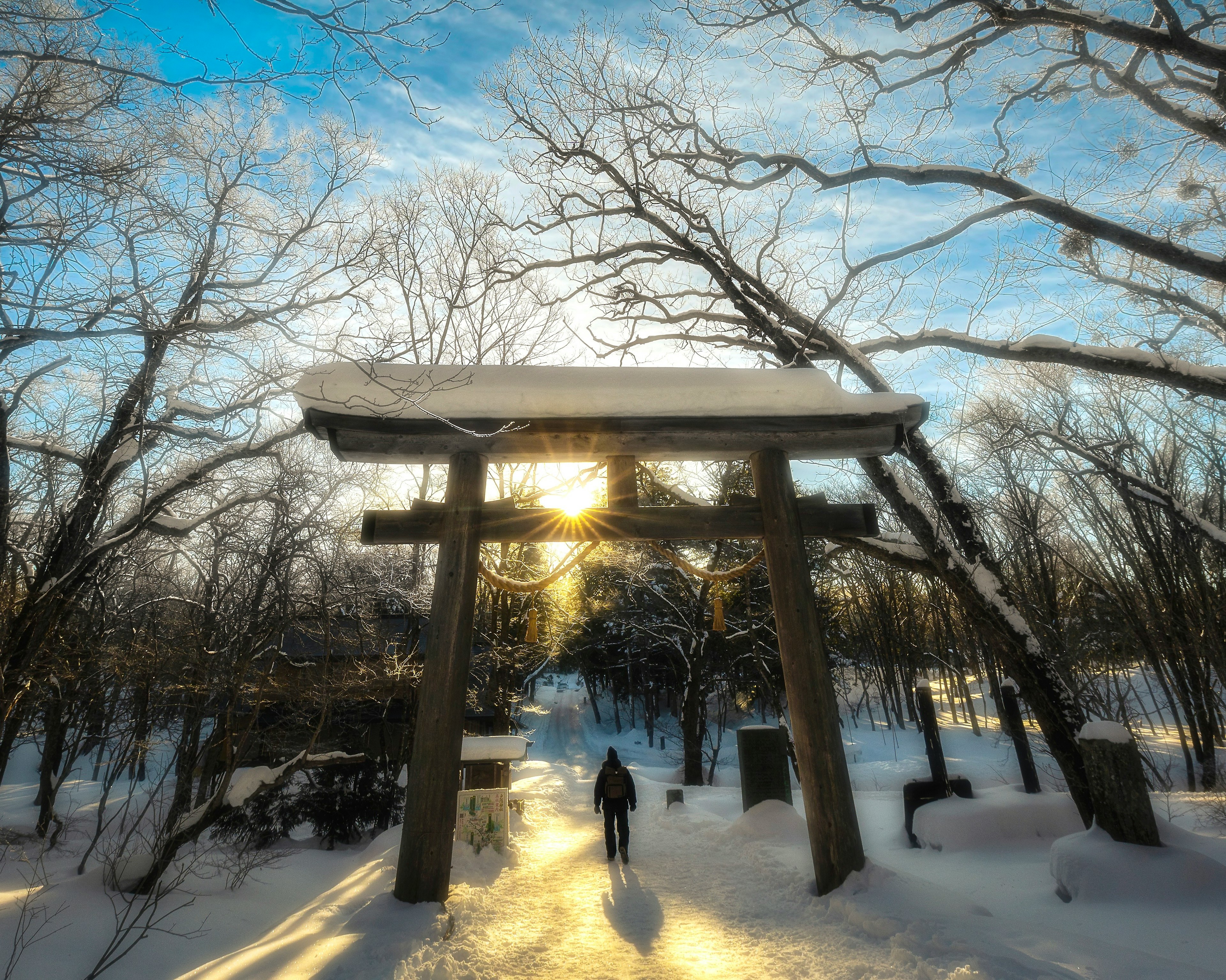 Person geht vor einem schneebedeckten Torii-Tor mit winterlichen Bäumen