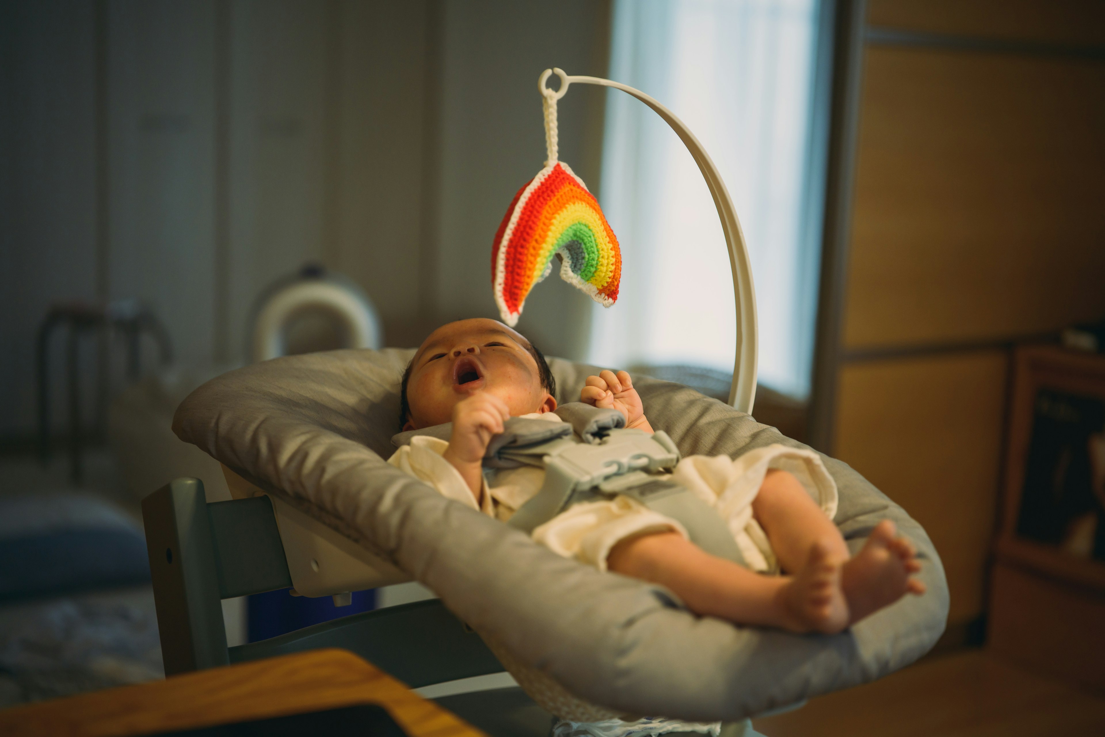 Seorang bayi tidur di bawah mainan gantung pelangi