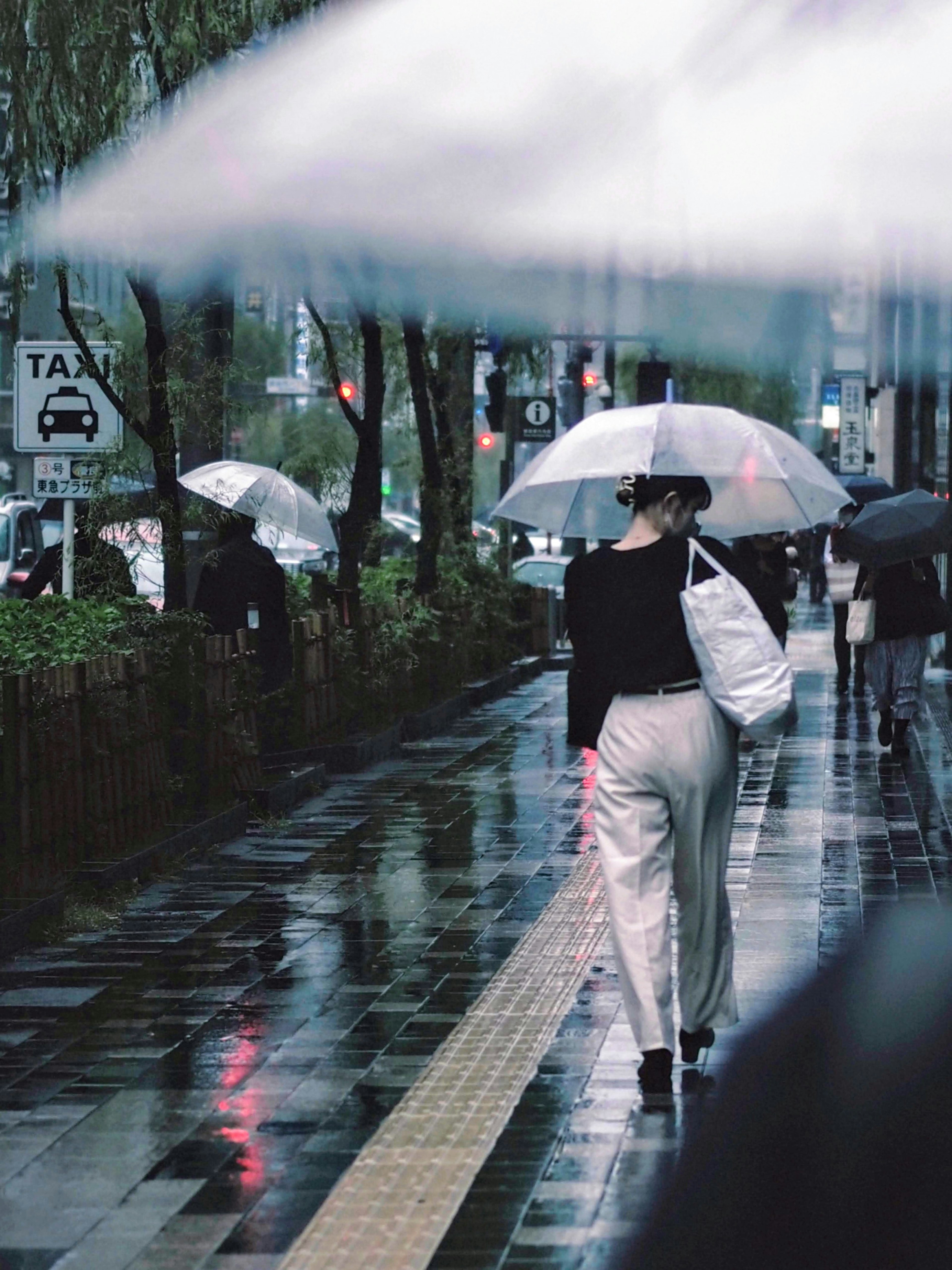 ผู้หญิงเดินในฝนถือร่มขาวสวมใส่ชุดดำบนพื้นผิวสะท้อนในเมือง