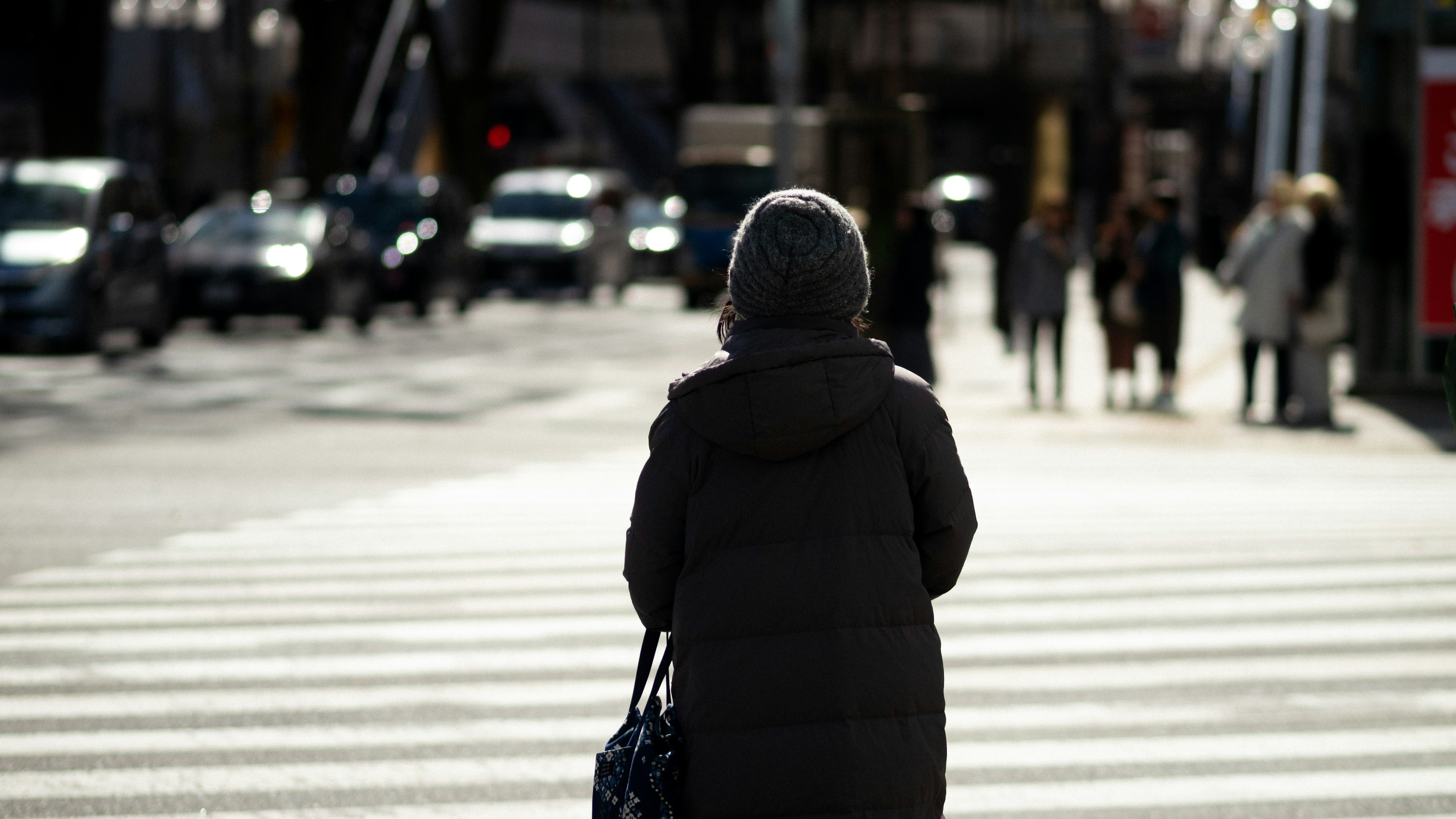 A woman walking on a crosswalk wearing a warm coat in a winter urban setting