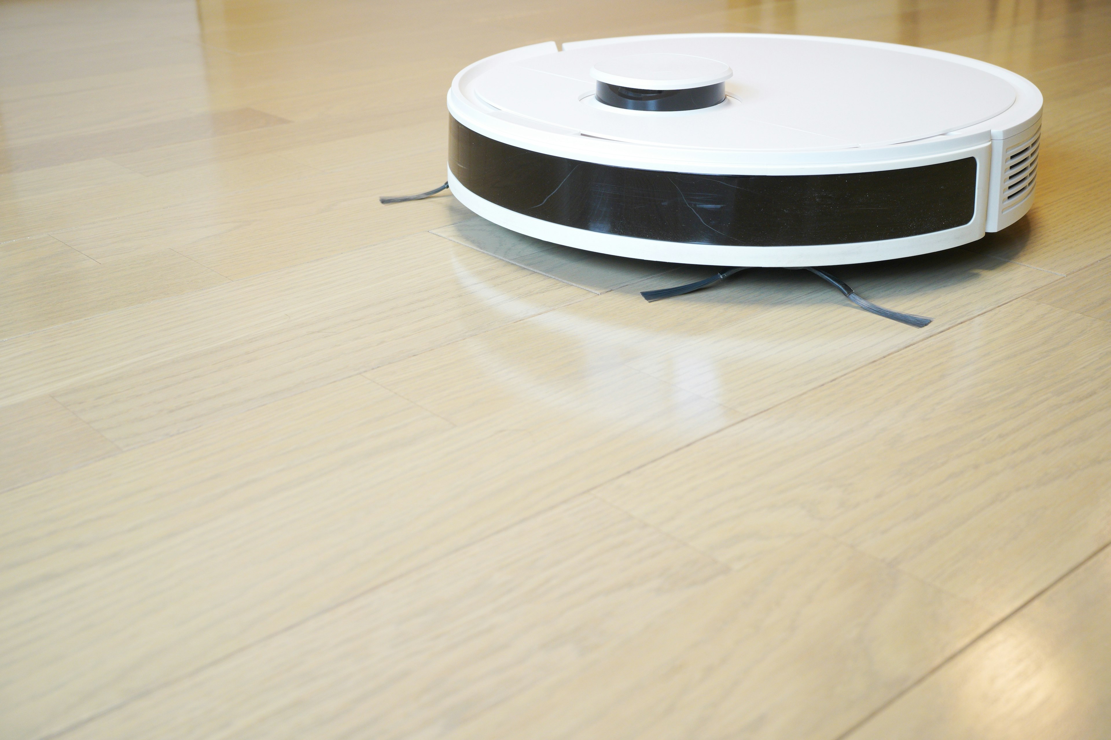 Aspirapolvere robot bianco che si muove su un pavimento in legno