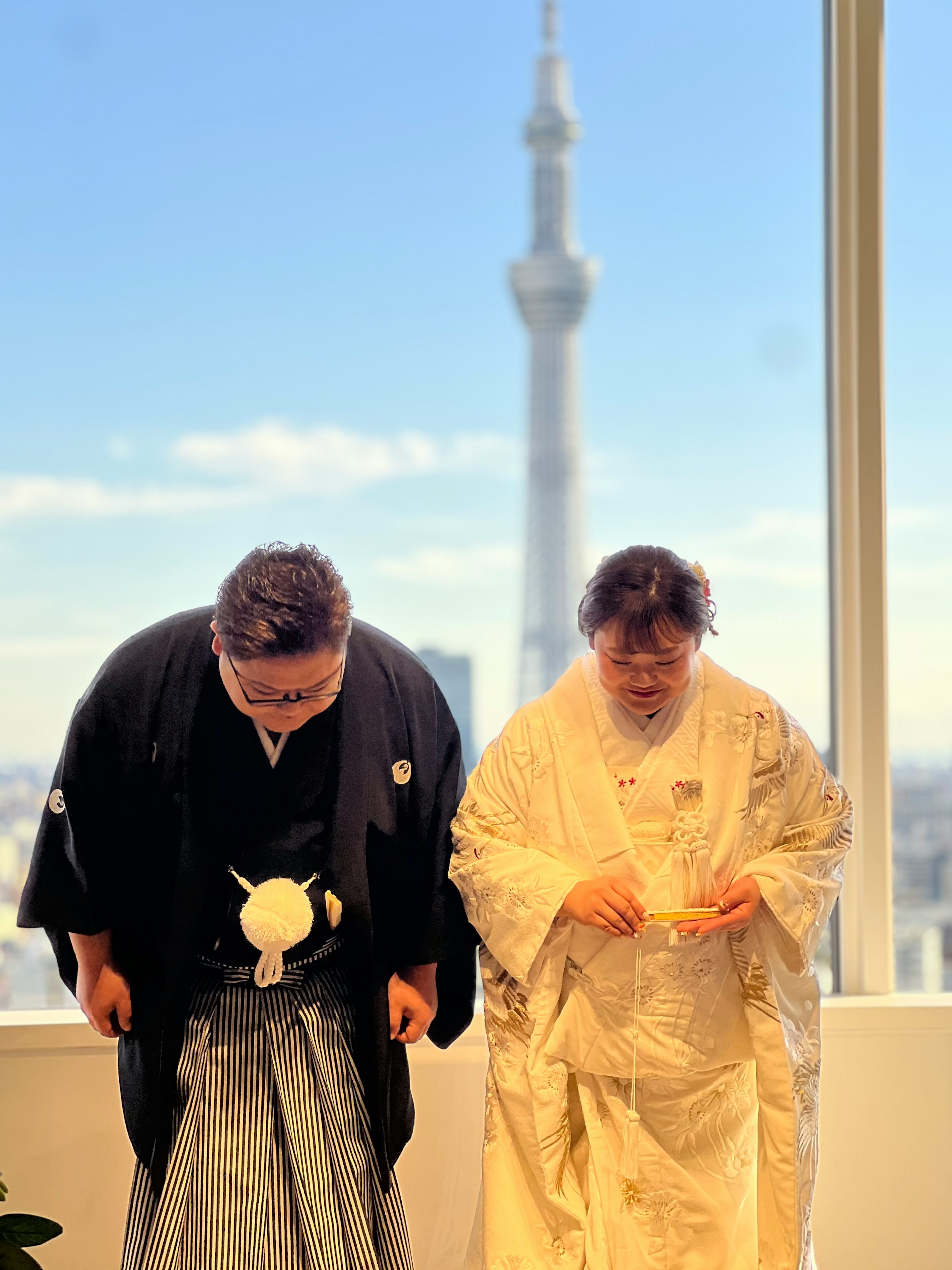 Deux personnes en vêtements traditionnels japonais s'inclinant avec la Tokyo Skytree en arrière-plan