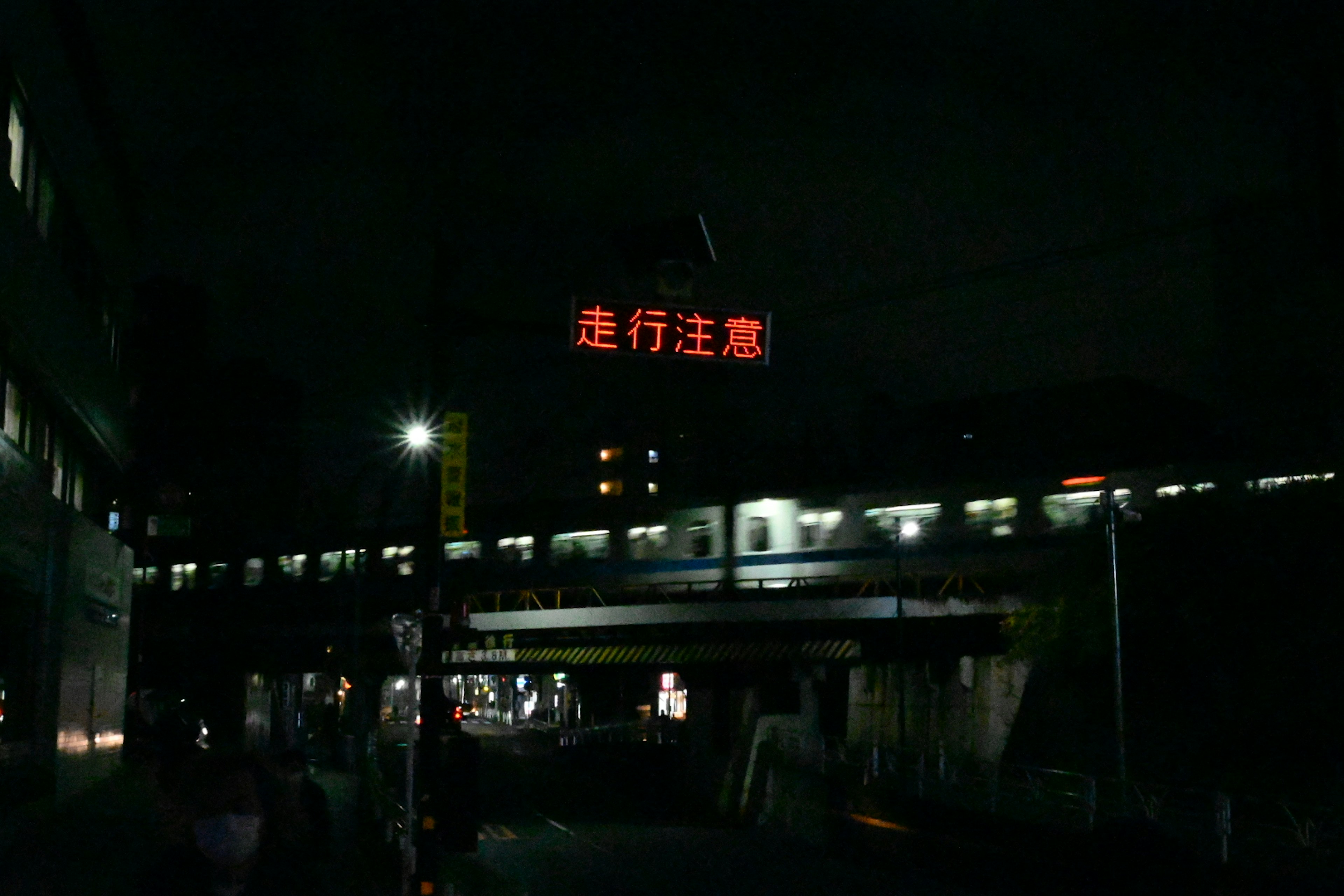 Train passant sous un pont la nuit avec un panneau d'avertissement rouge