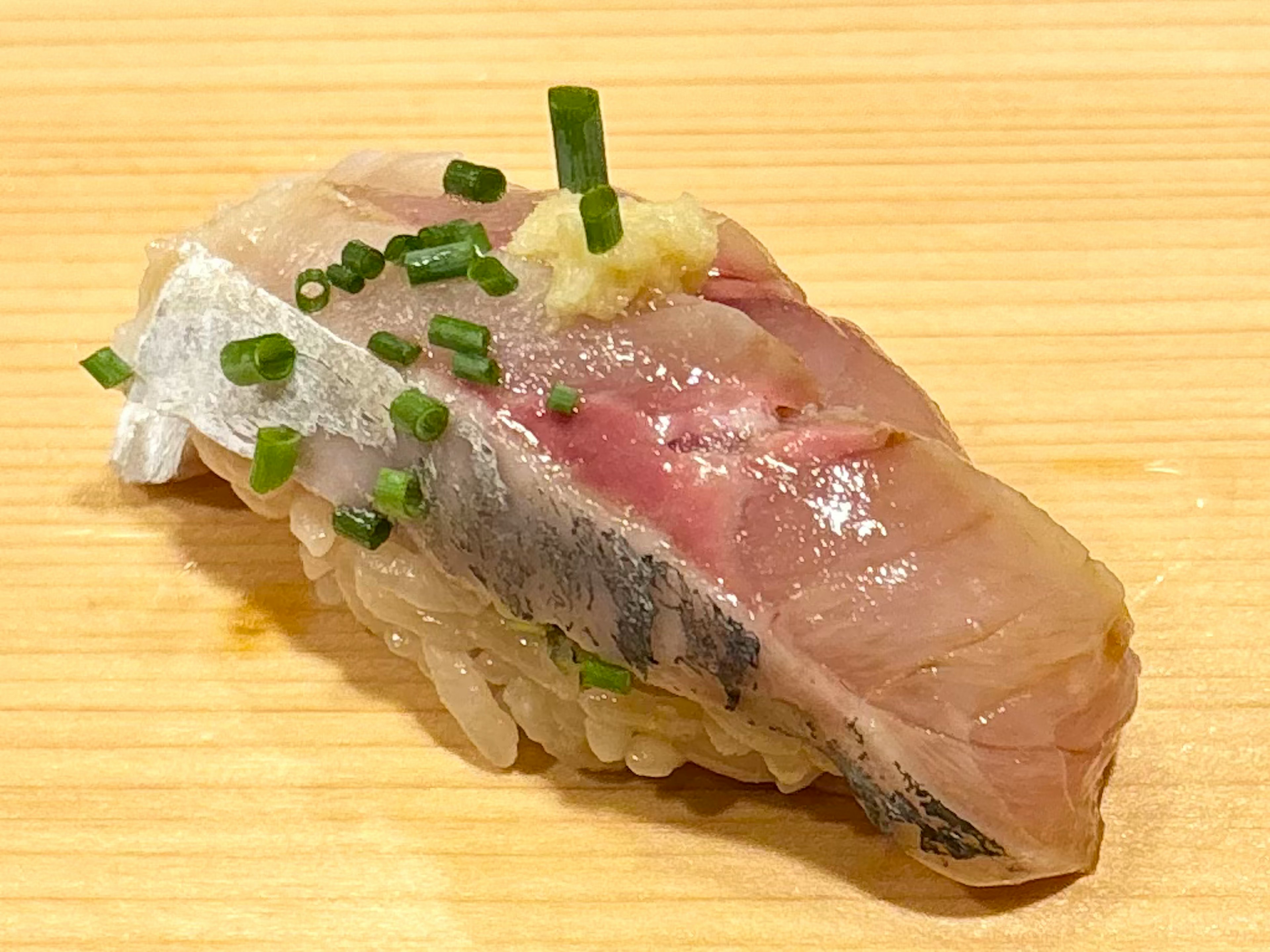 新鮮な魚の寿司の一片に青ねぎと生姜がトッピングされています