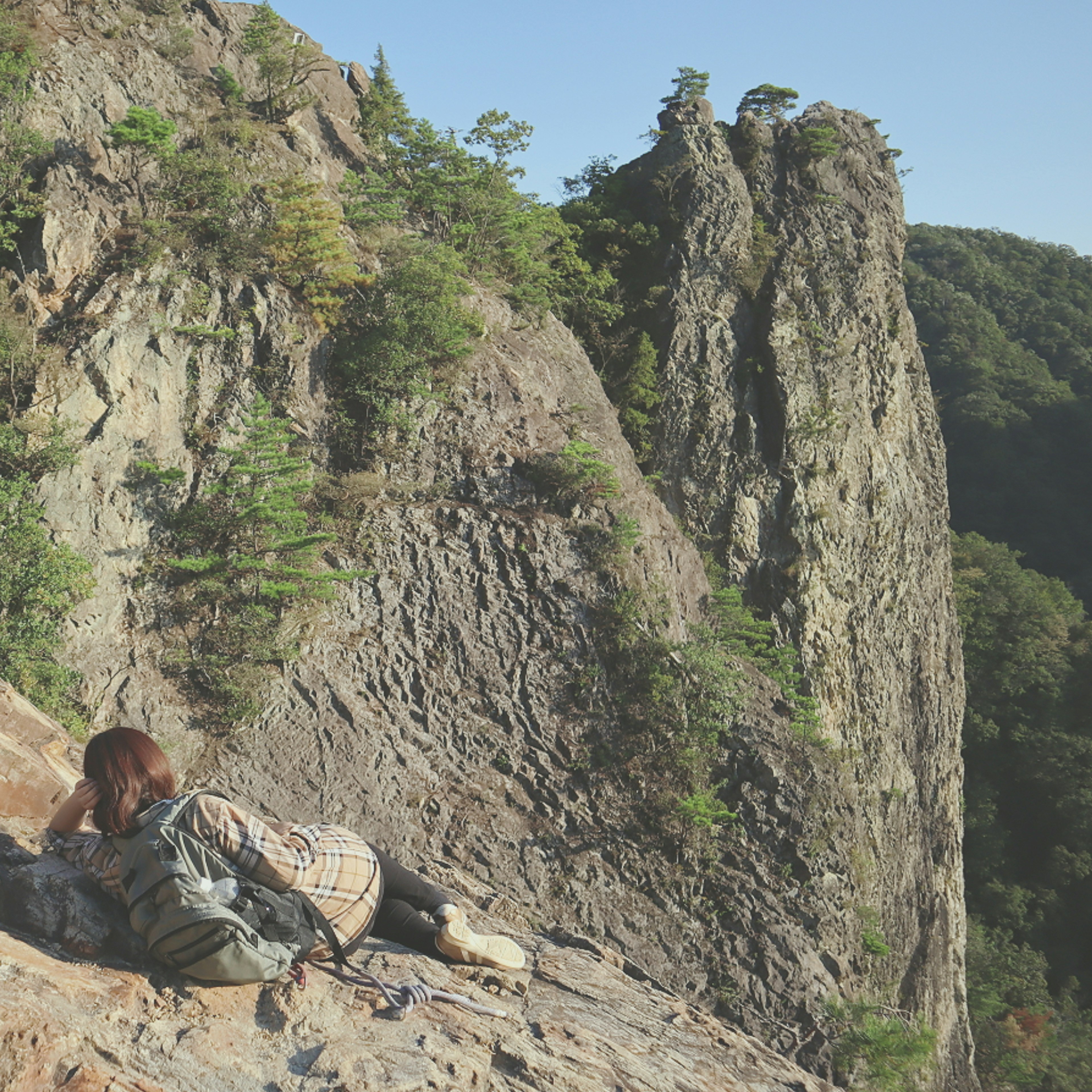 A woman lying on a rock in a hiking scene featuring lush forest and pointed rock formations