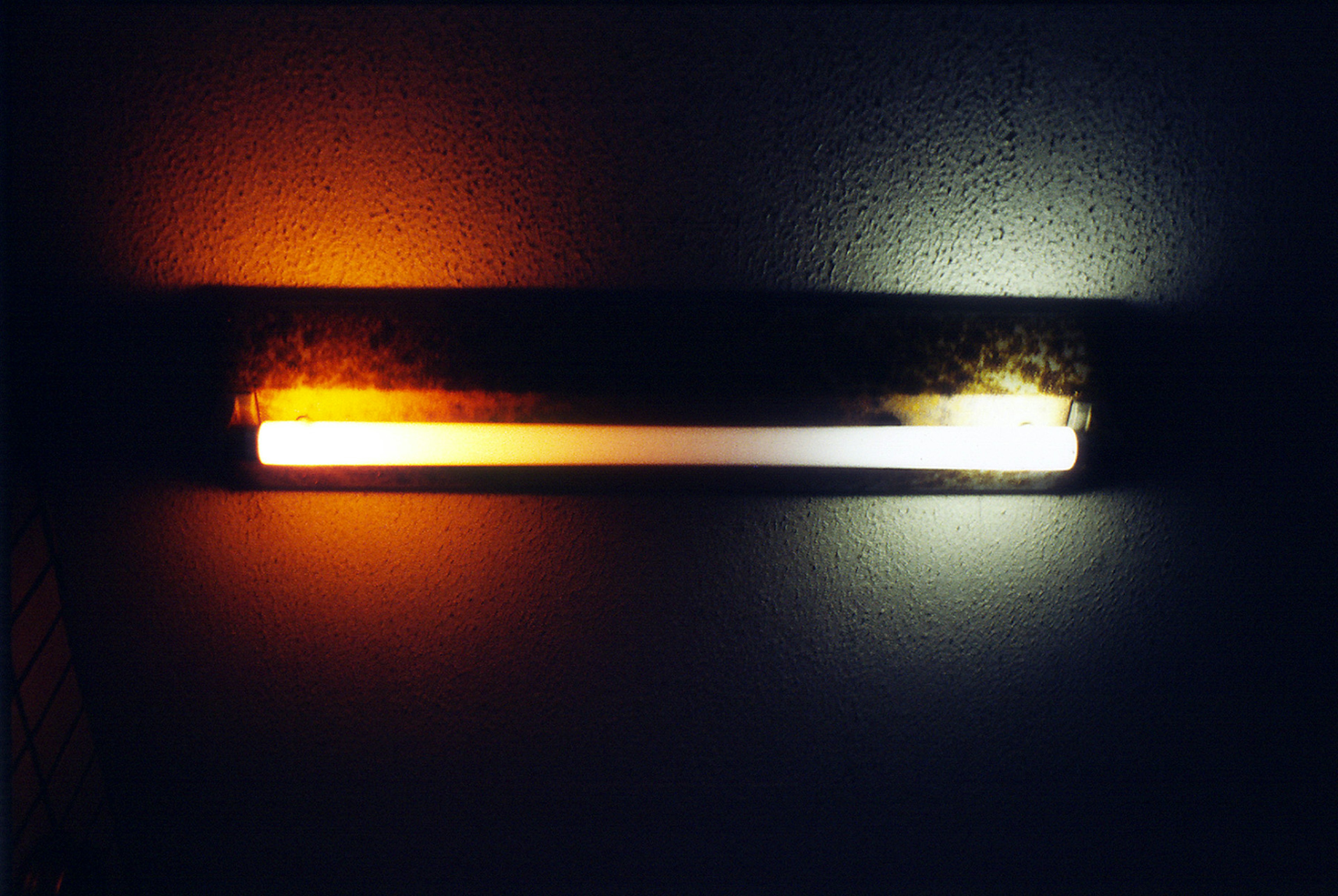 Two fluorescent lights emitting orange and white light mounted on a wall