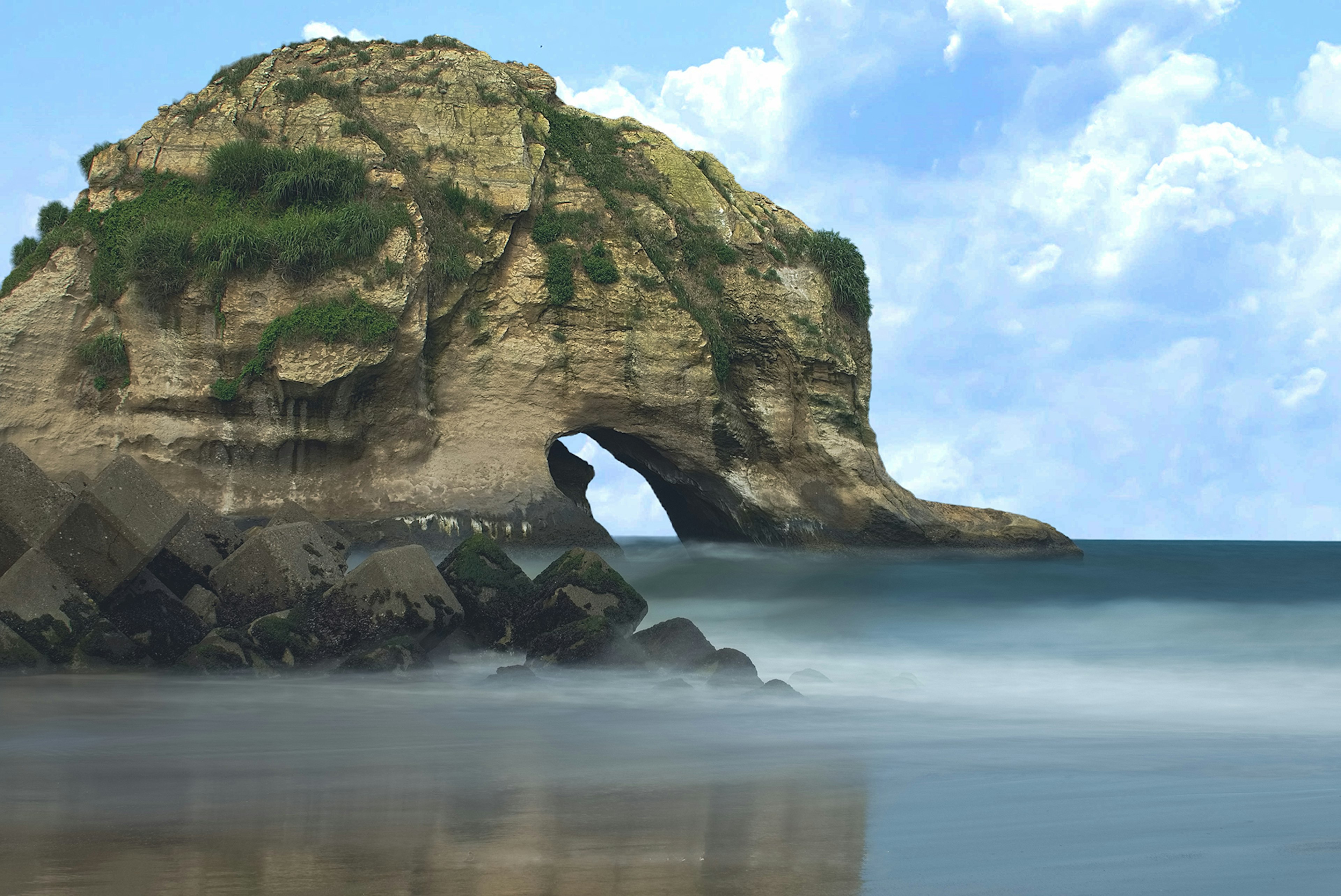 Grande formation rocheuse dans la mer avec une arche naturelle et un ciel bleu