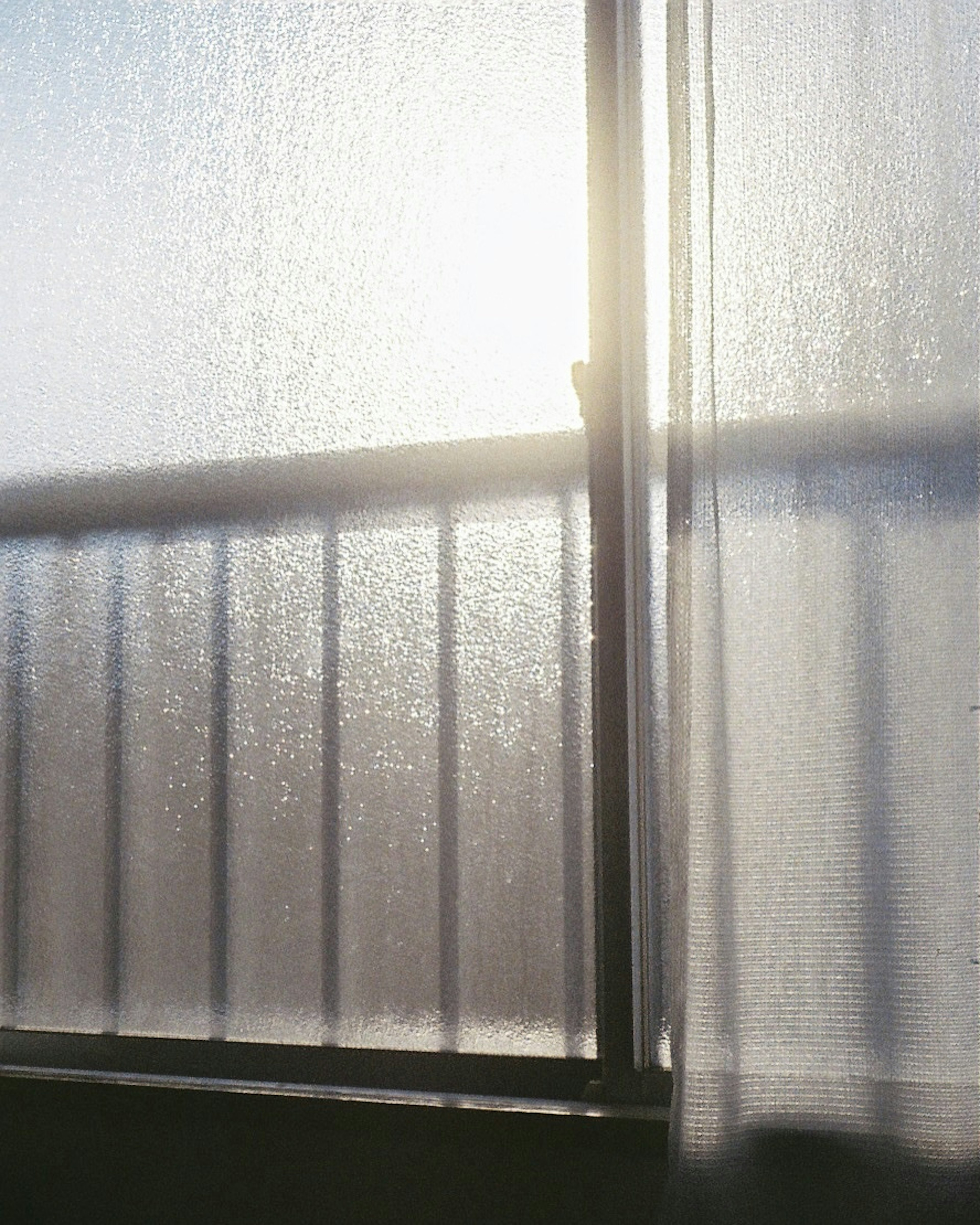 Soft sunlight filtering through a curtain with water droplets on the window