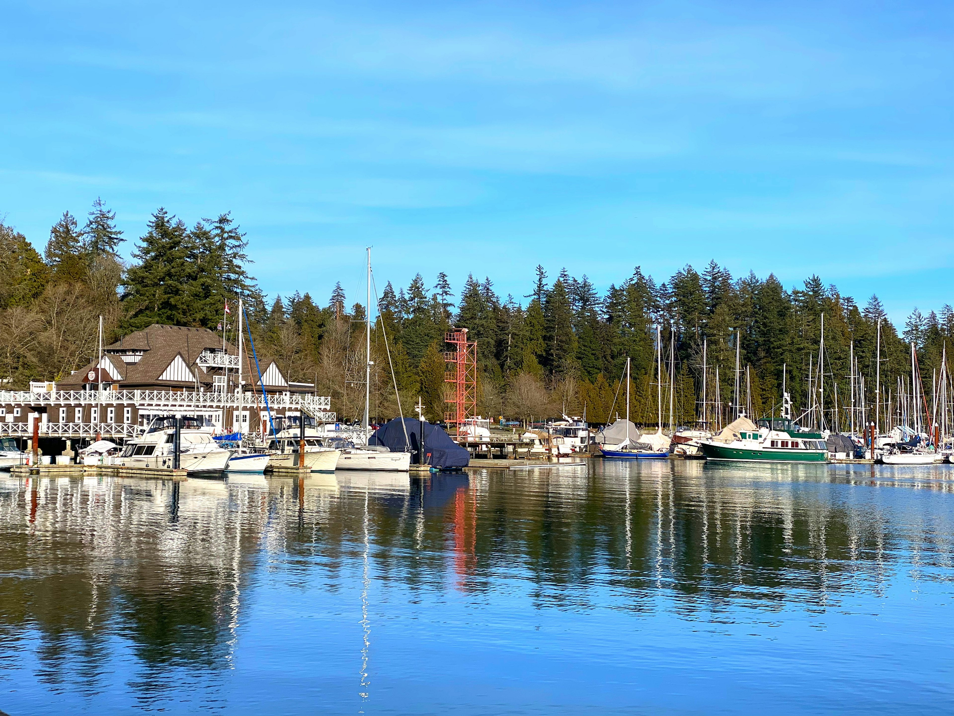 Vue pittoresque d'un port de plaisance avec des bateaux et un phare entouré d'arbres et d'un ciel bleu