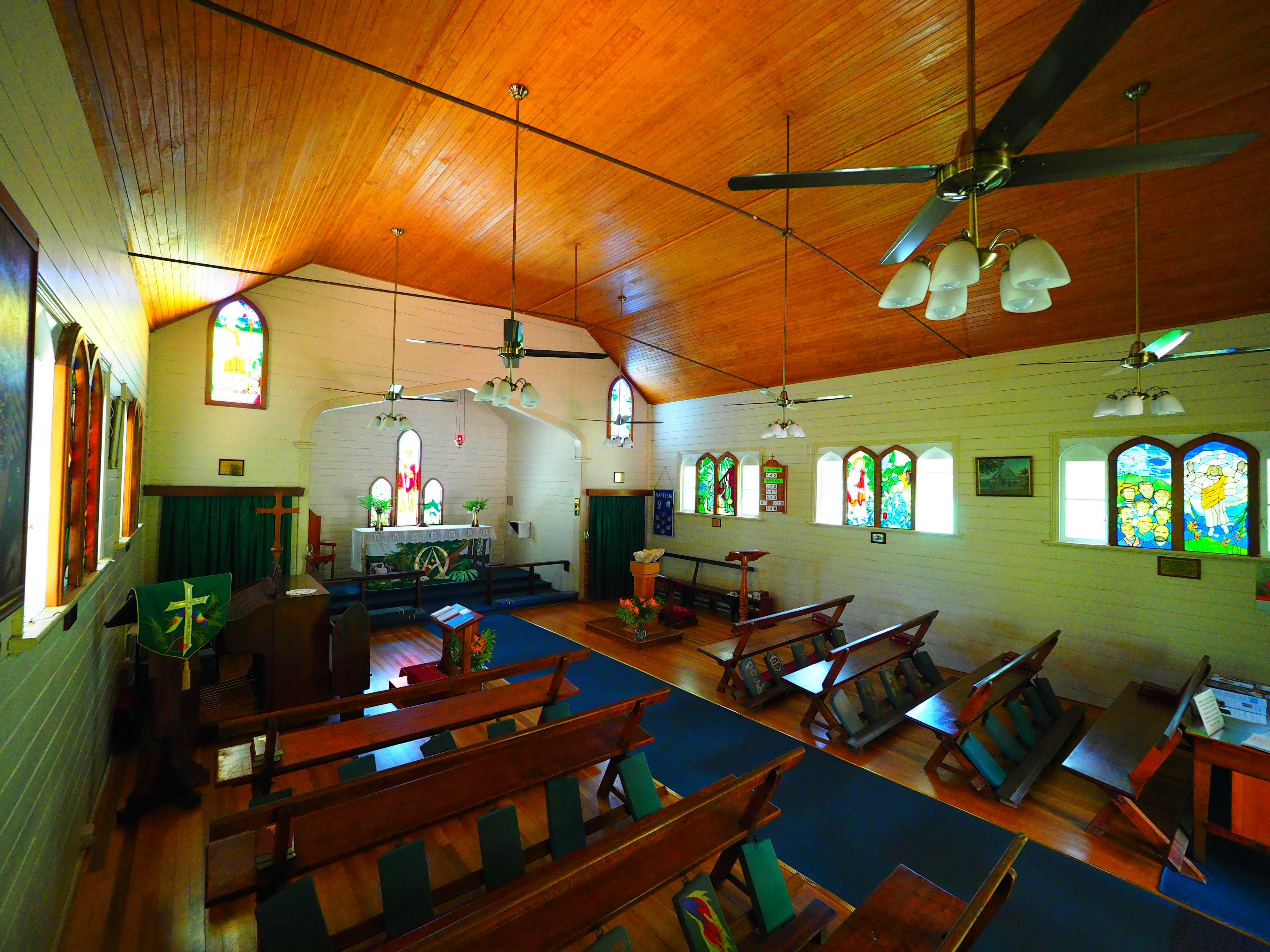 Intérieur d'église lumineux avec fenêtres en vitrail bancs en bois et disposition spacieuse ventilateurs de plafond