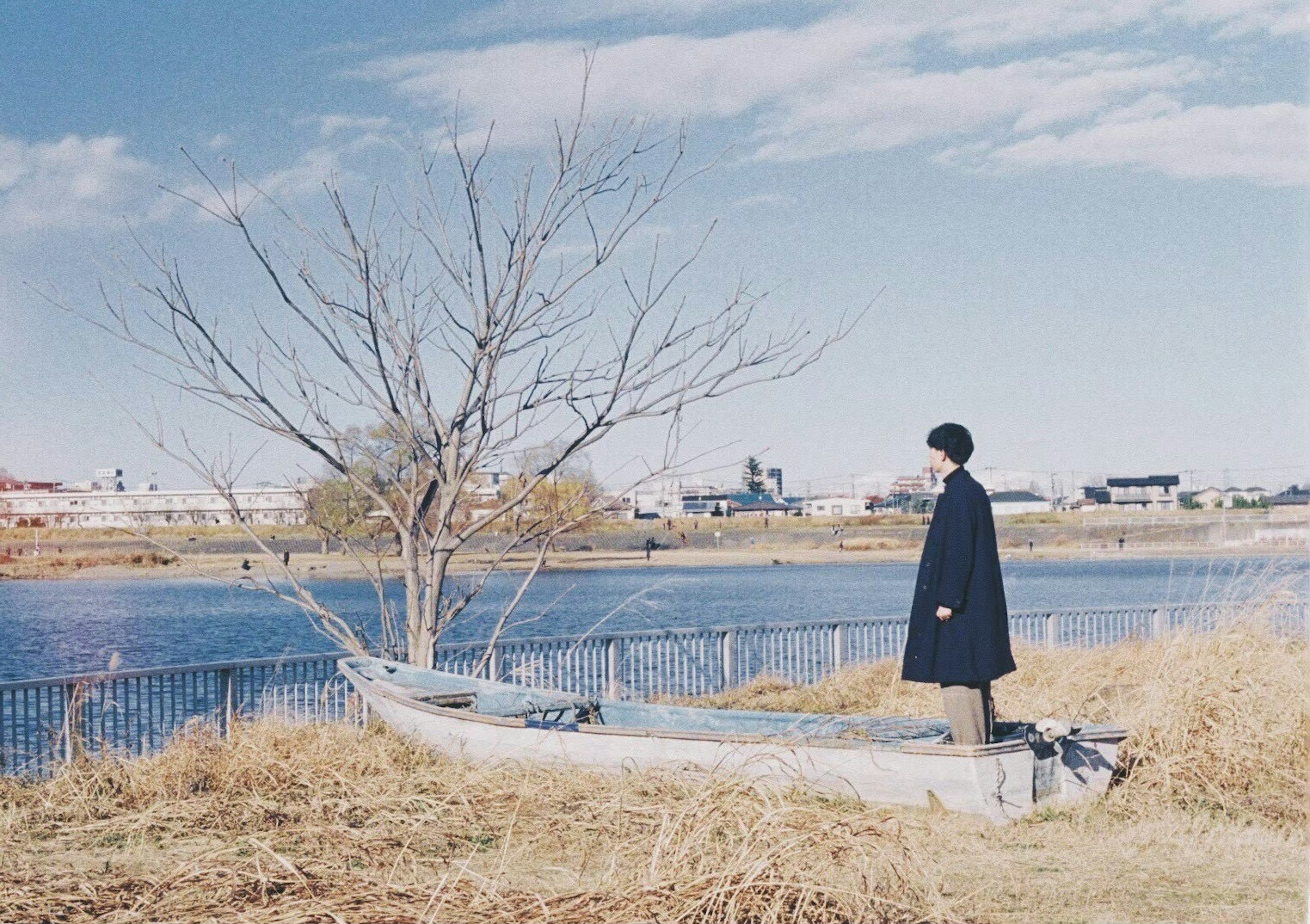 A person standing by a river with a bare tree and blue sky