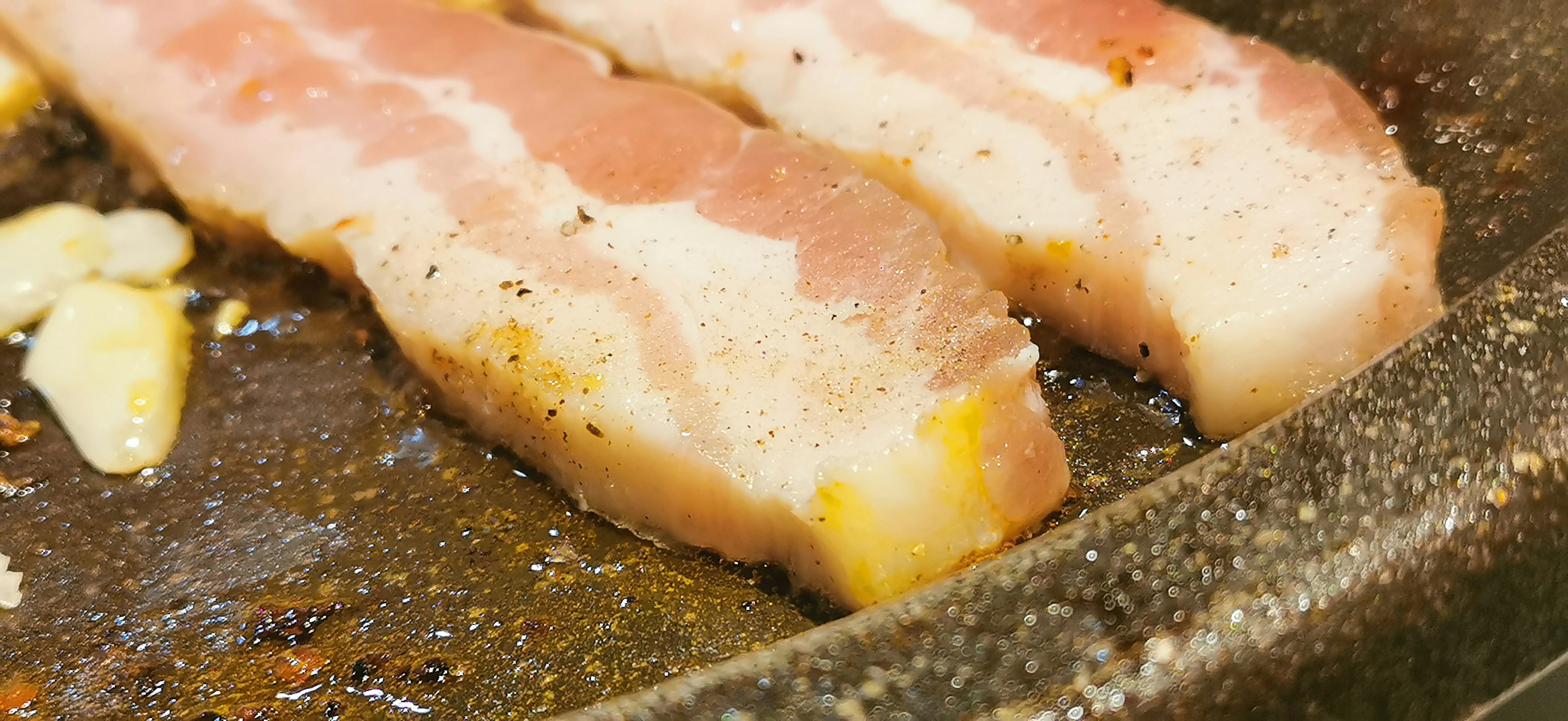 Slices of pork belly cooking in a frying pan