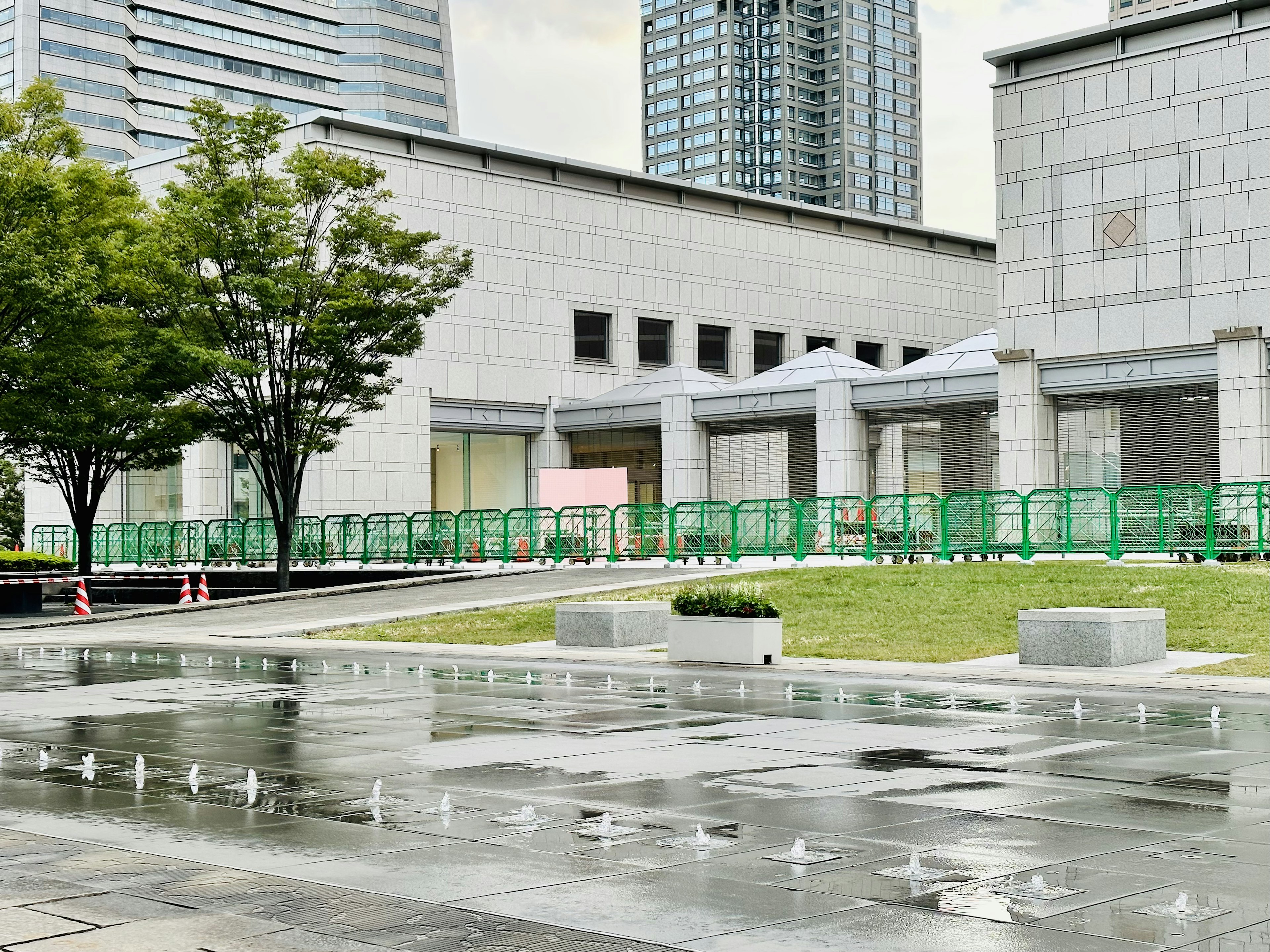 現代的な建物の前の広場にある水の噴水と緑のフェンス