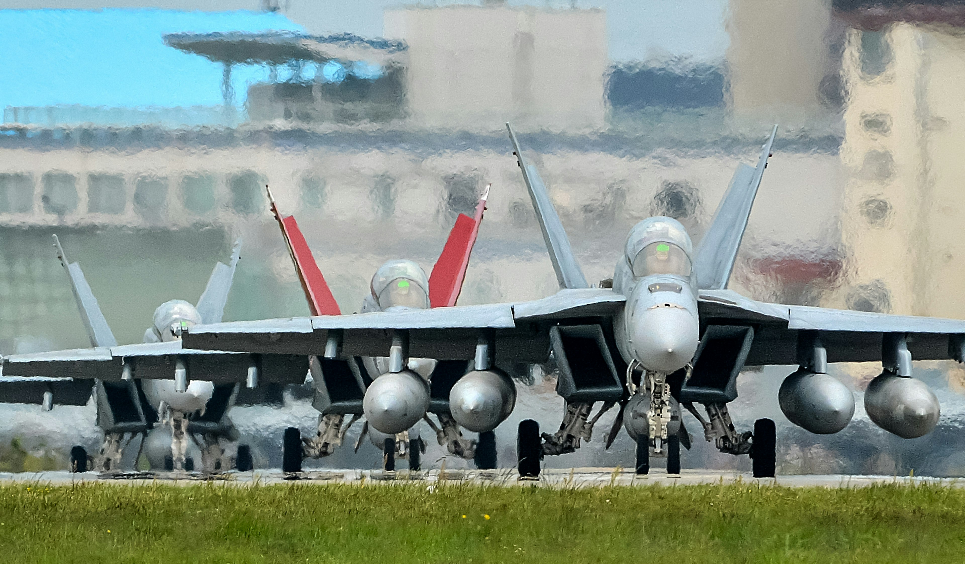 A lineup of military fighter jets on a runway with an airport in the background