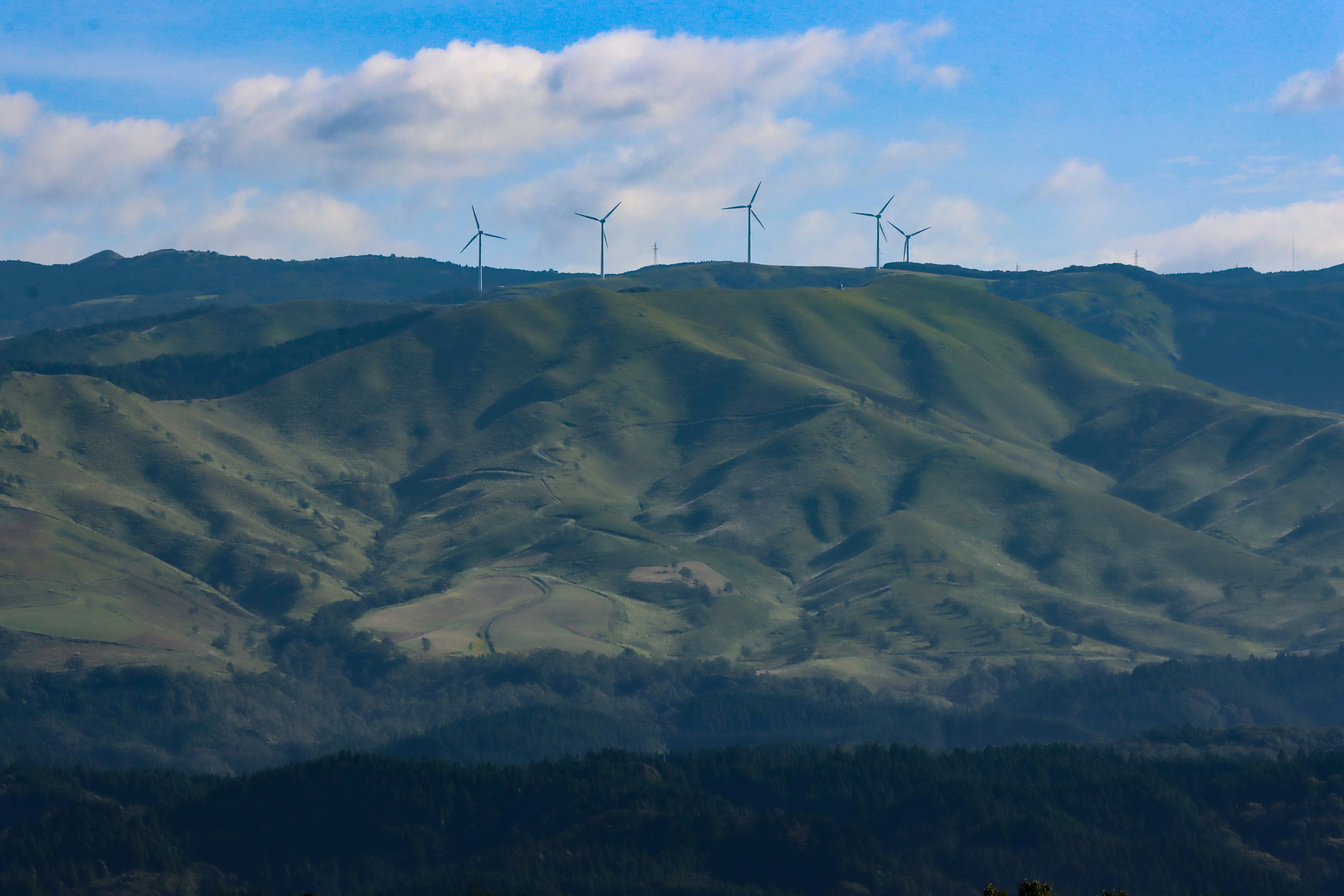 風力発電機が並ぶ緑の山々と青い空の風景