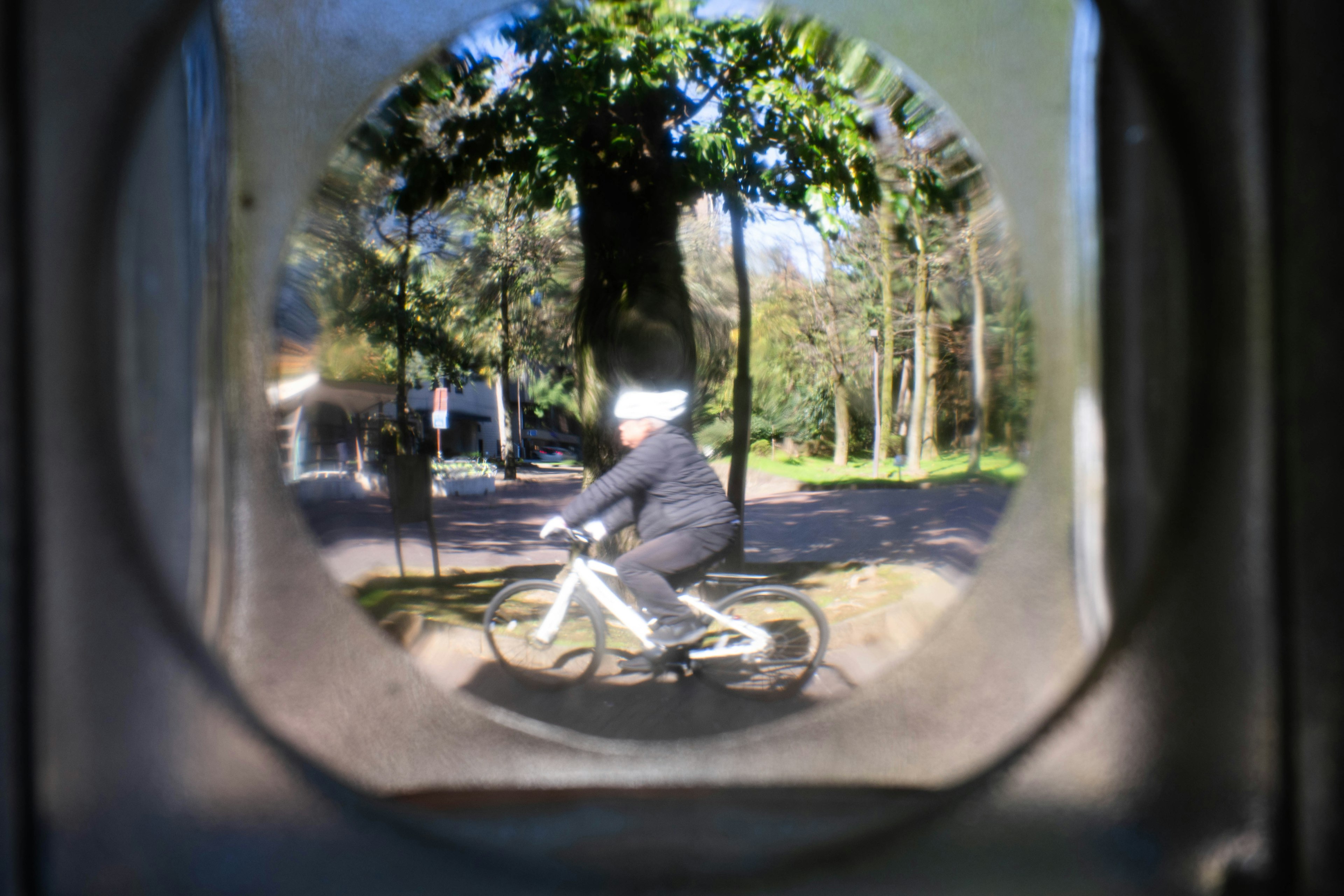 Un niño montando una bicicleta visto a través de una abertura circular en un parque