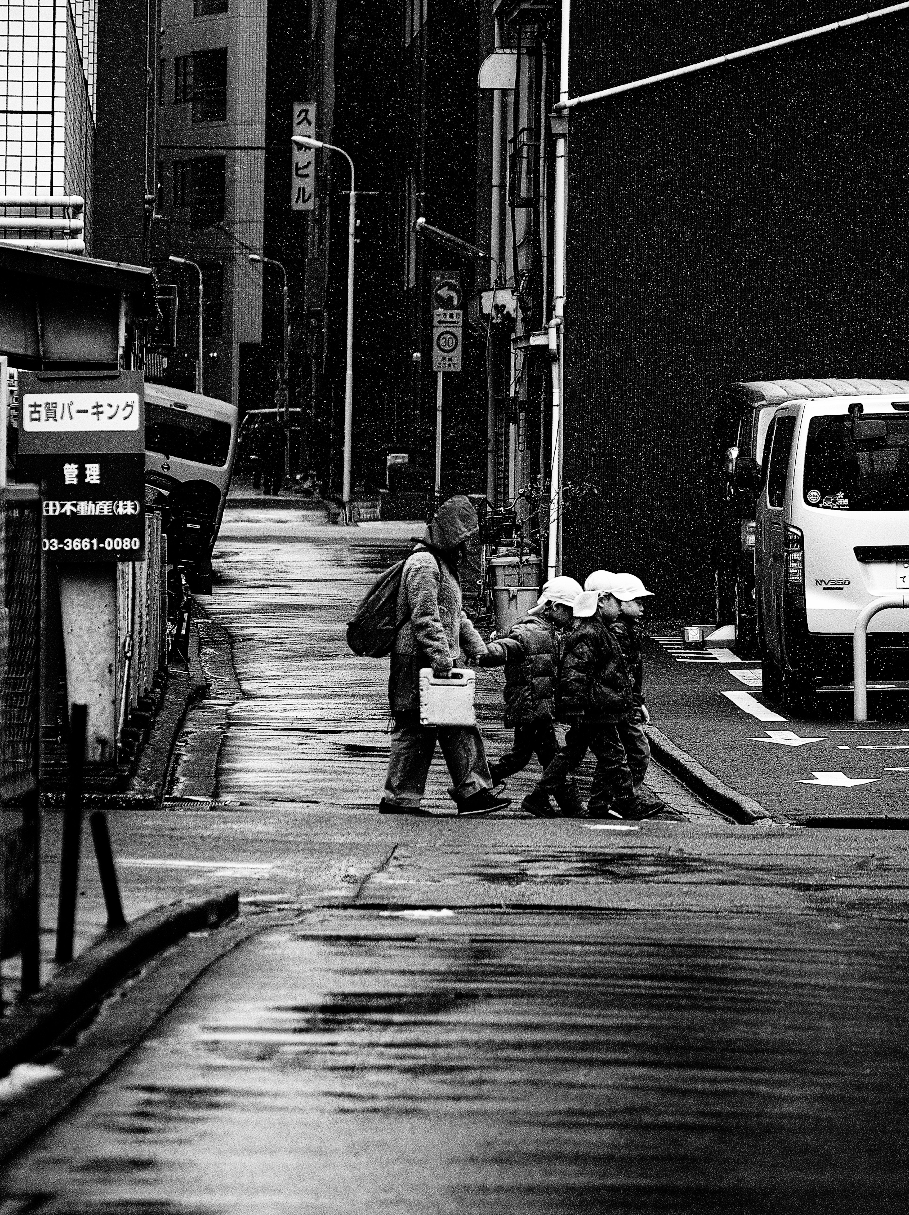 Photo en noir et blanc d'un adulte marchant avec des enfants sous la pluie