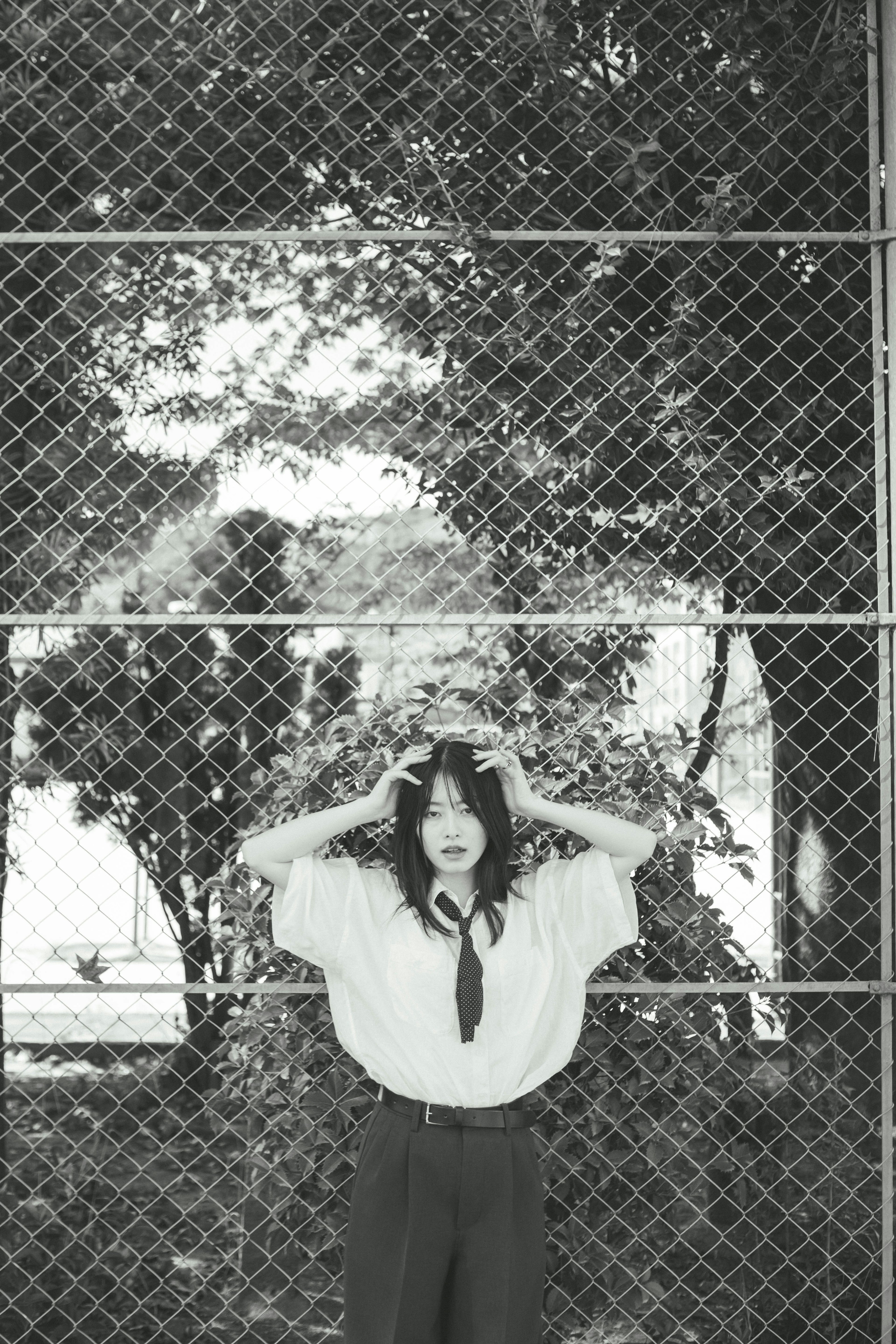 Black and white photo of a woman holding her head in front of a fence