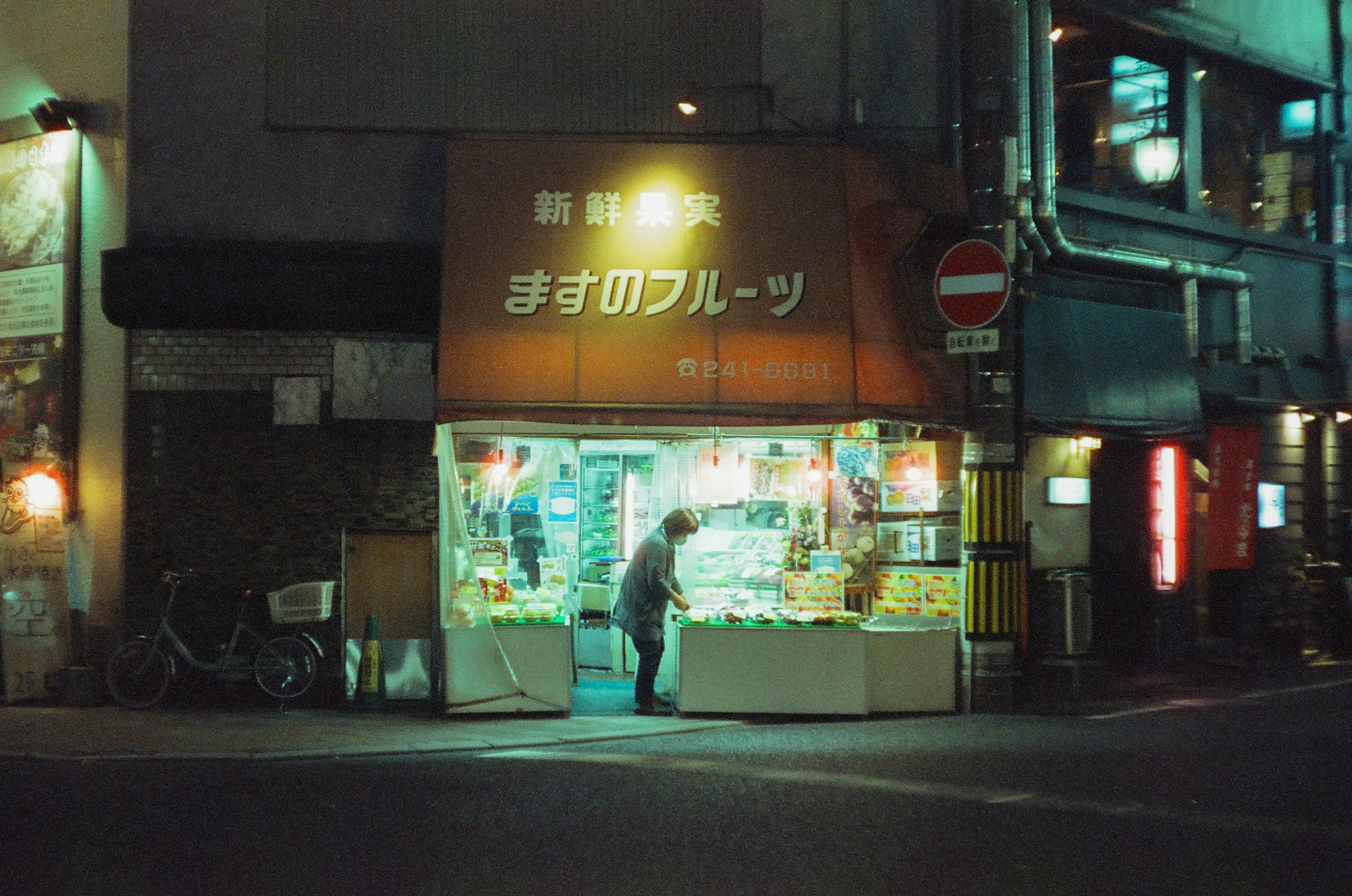 夜の街角にあるフルーツショップの外観と店員