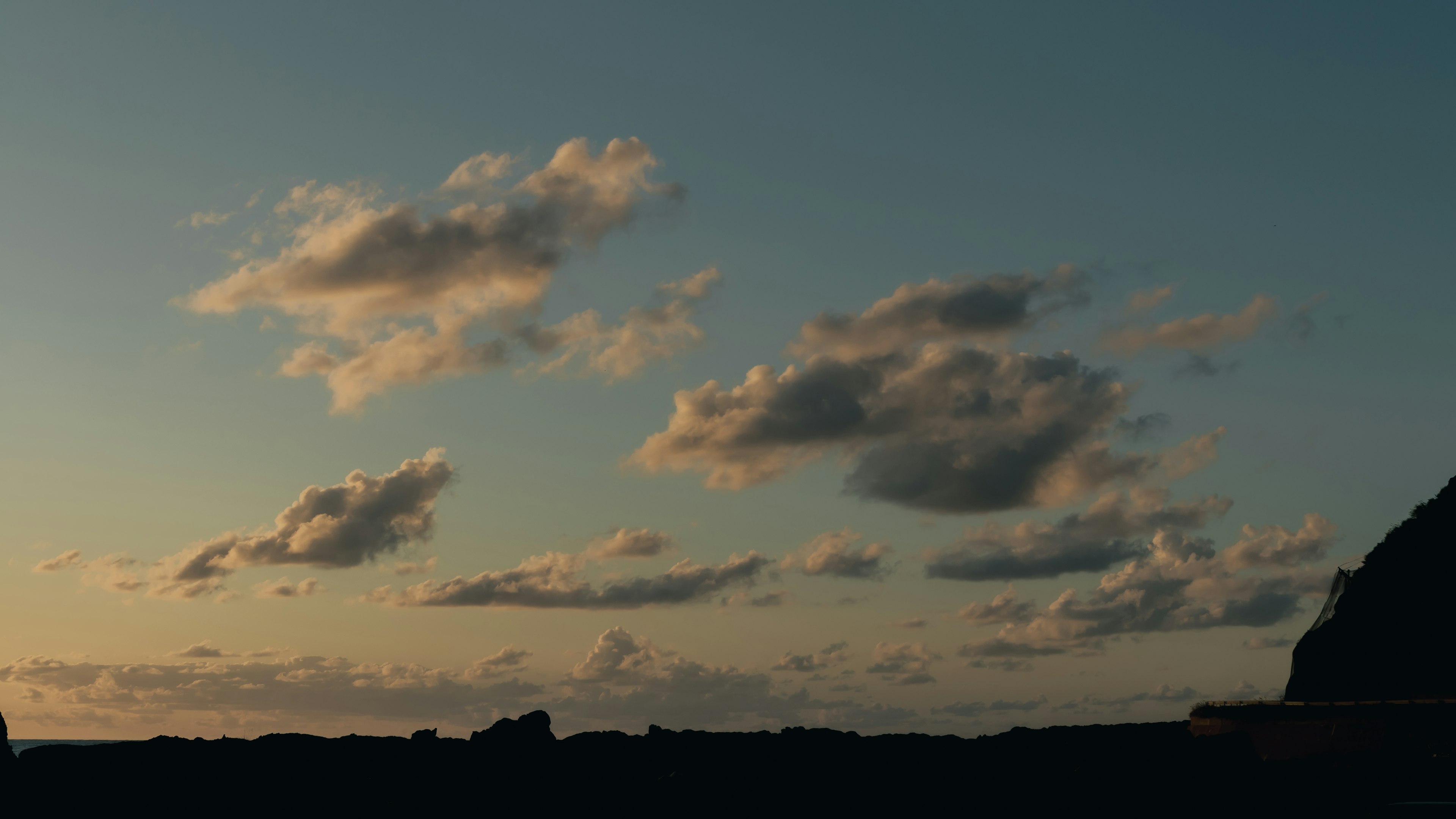 夕焼けの空に浮かぶ雲と影のある山のシルエット