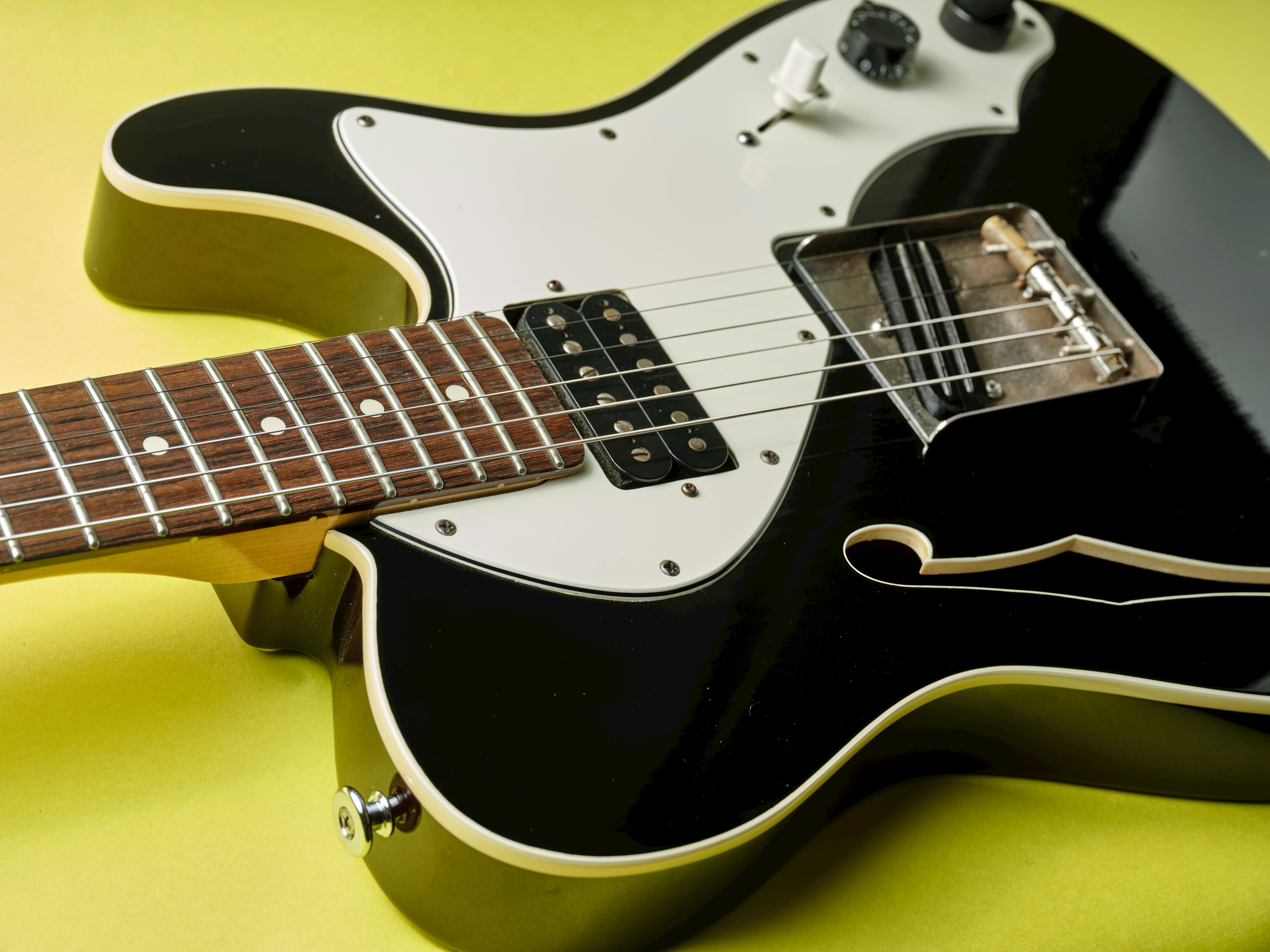 Foto close-up gitar listrik hitam dengan fretboard kayu dan pickguard putih