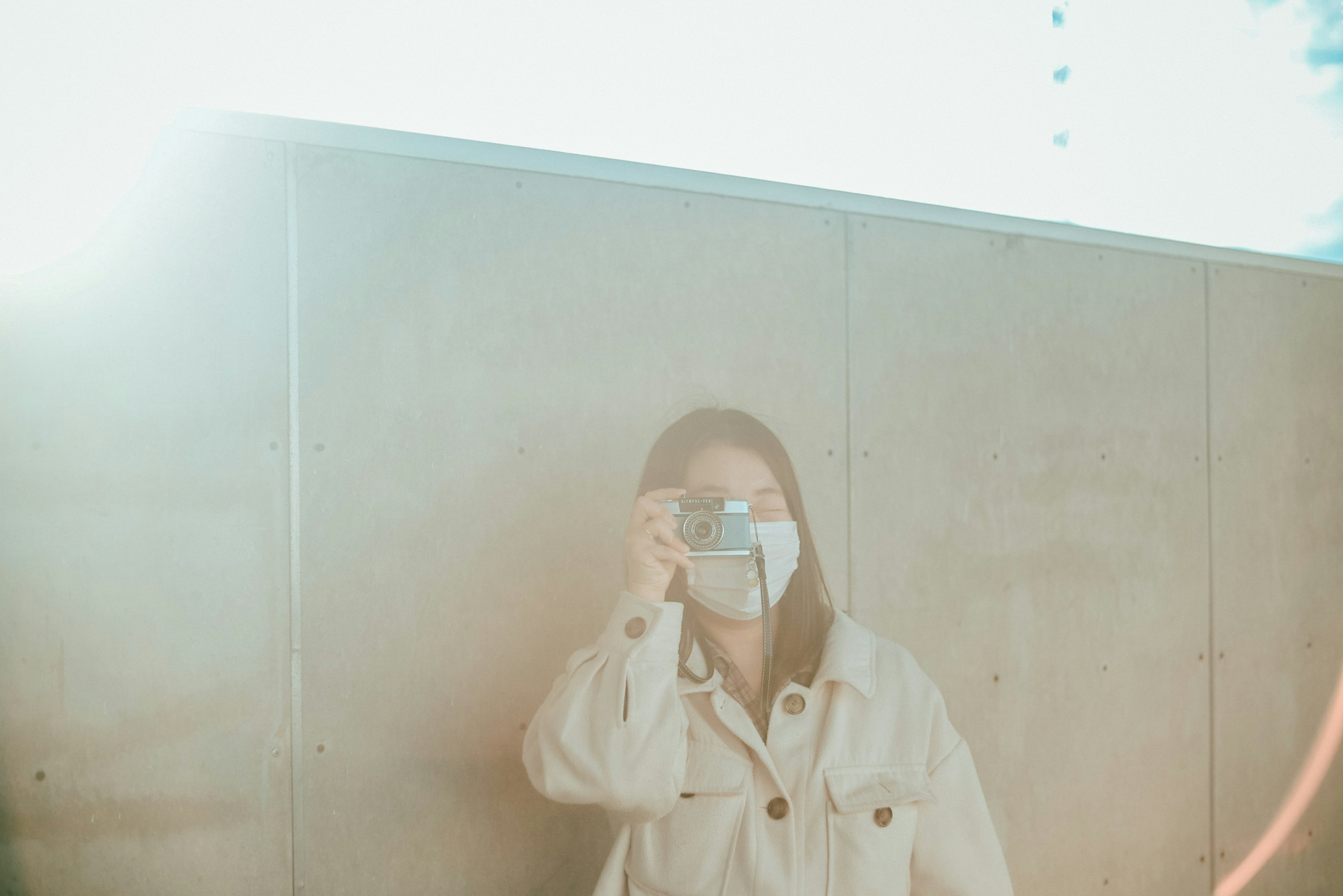 A woman posing with a camera in front of a concrete wall