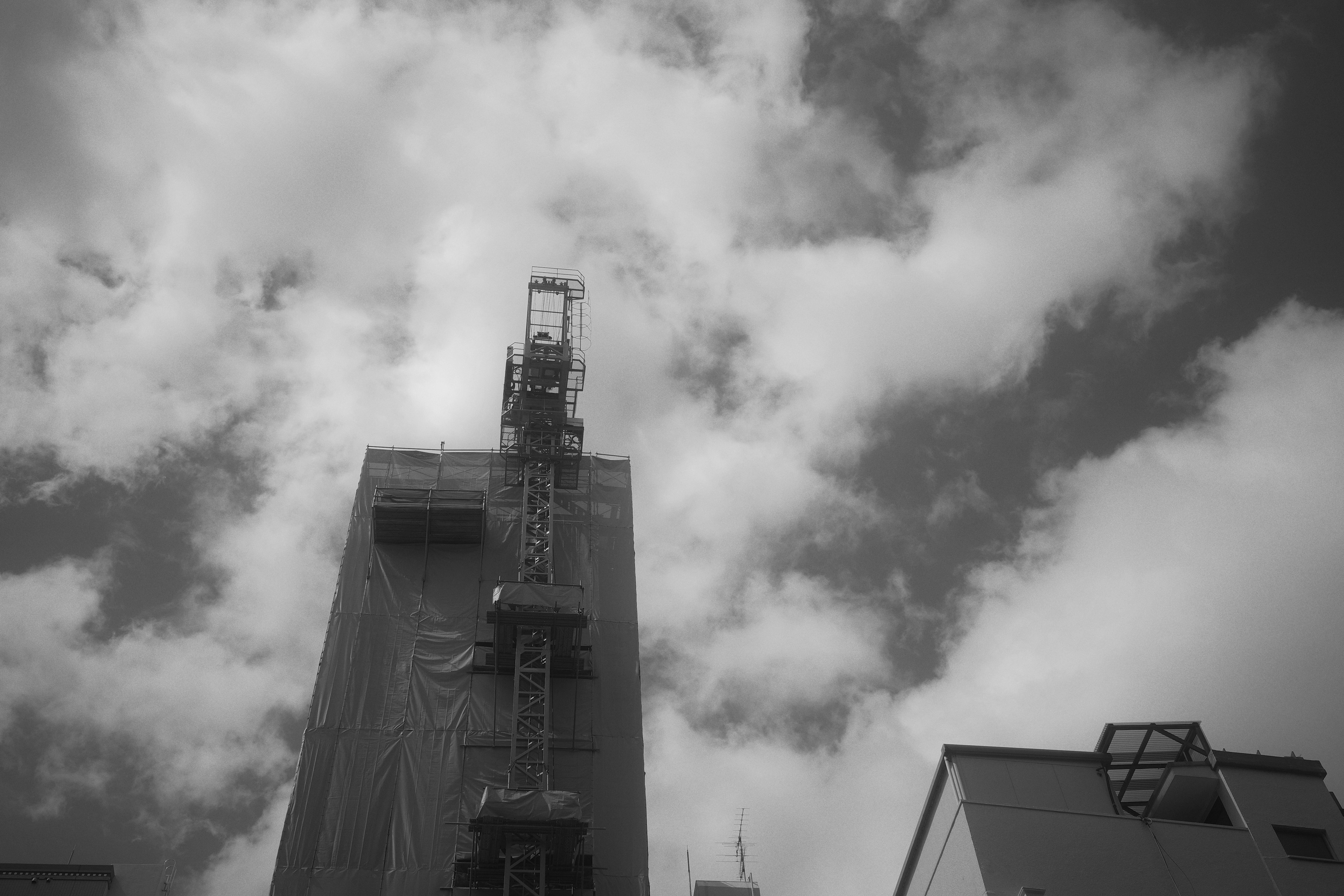 高層建築上的施工起重機與多雲的天空