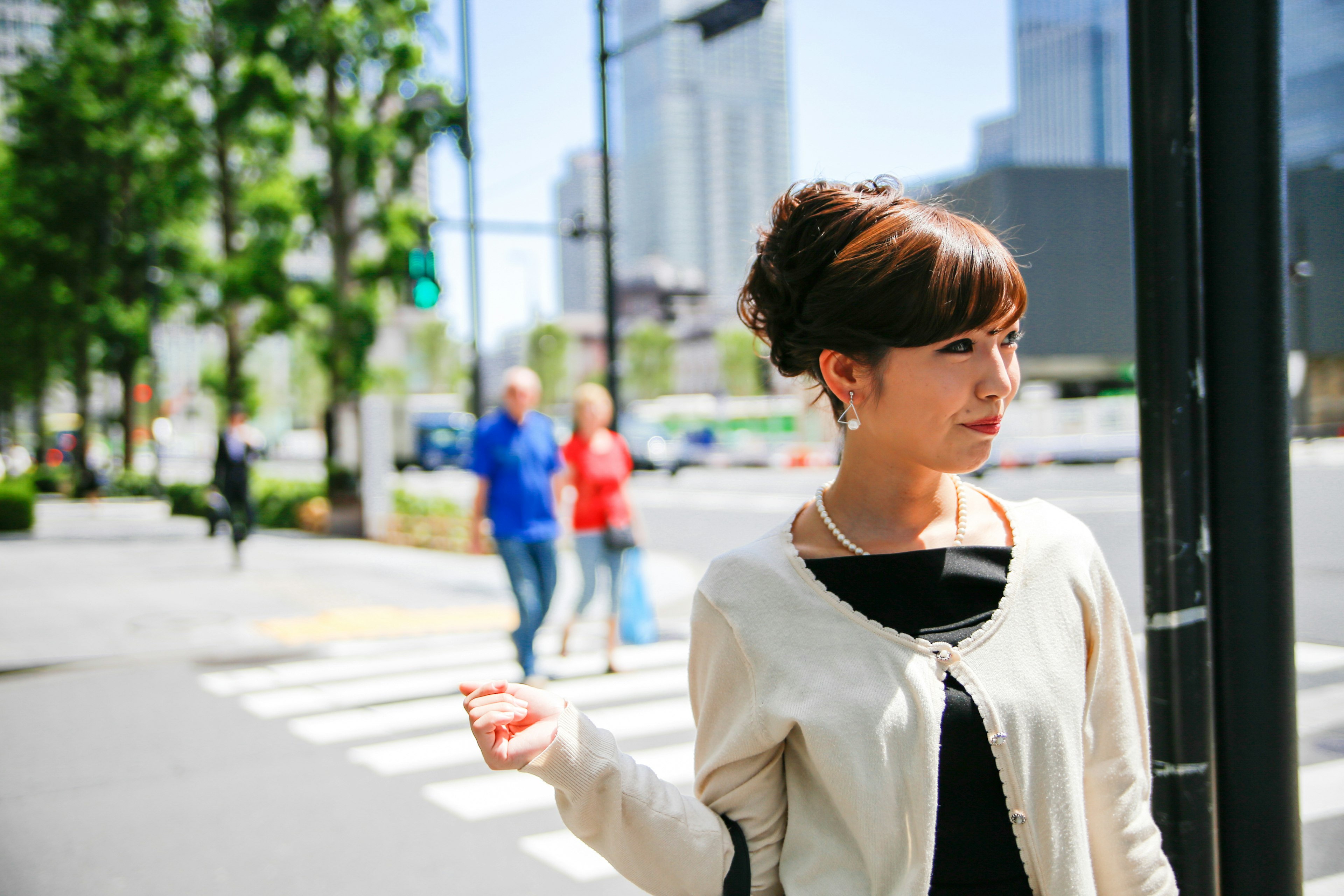 Woman standing at a city intersection casual attire modern buildings and green trees in the background