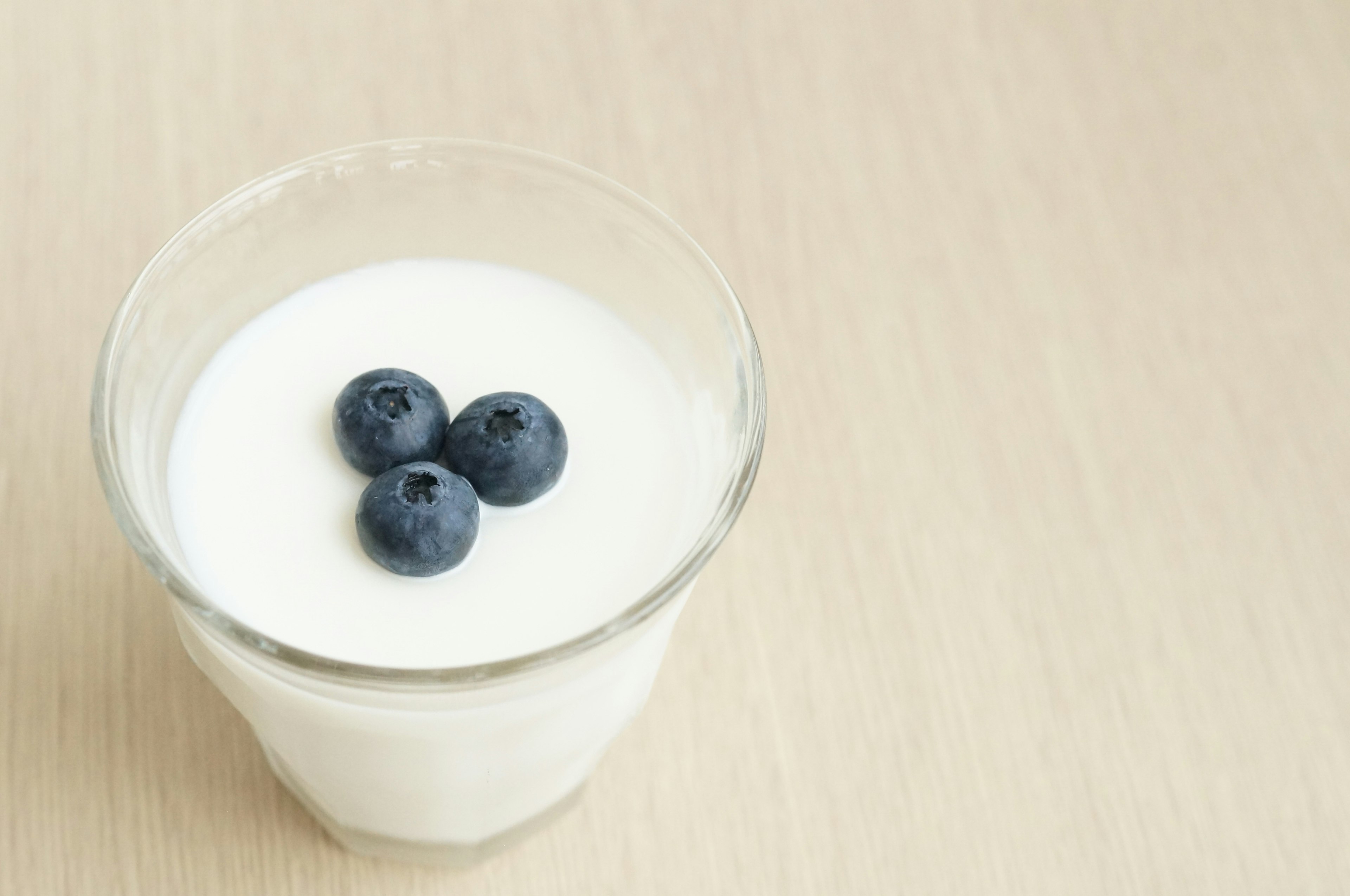 A clear glass containing yogurt topped with three blueberries