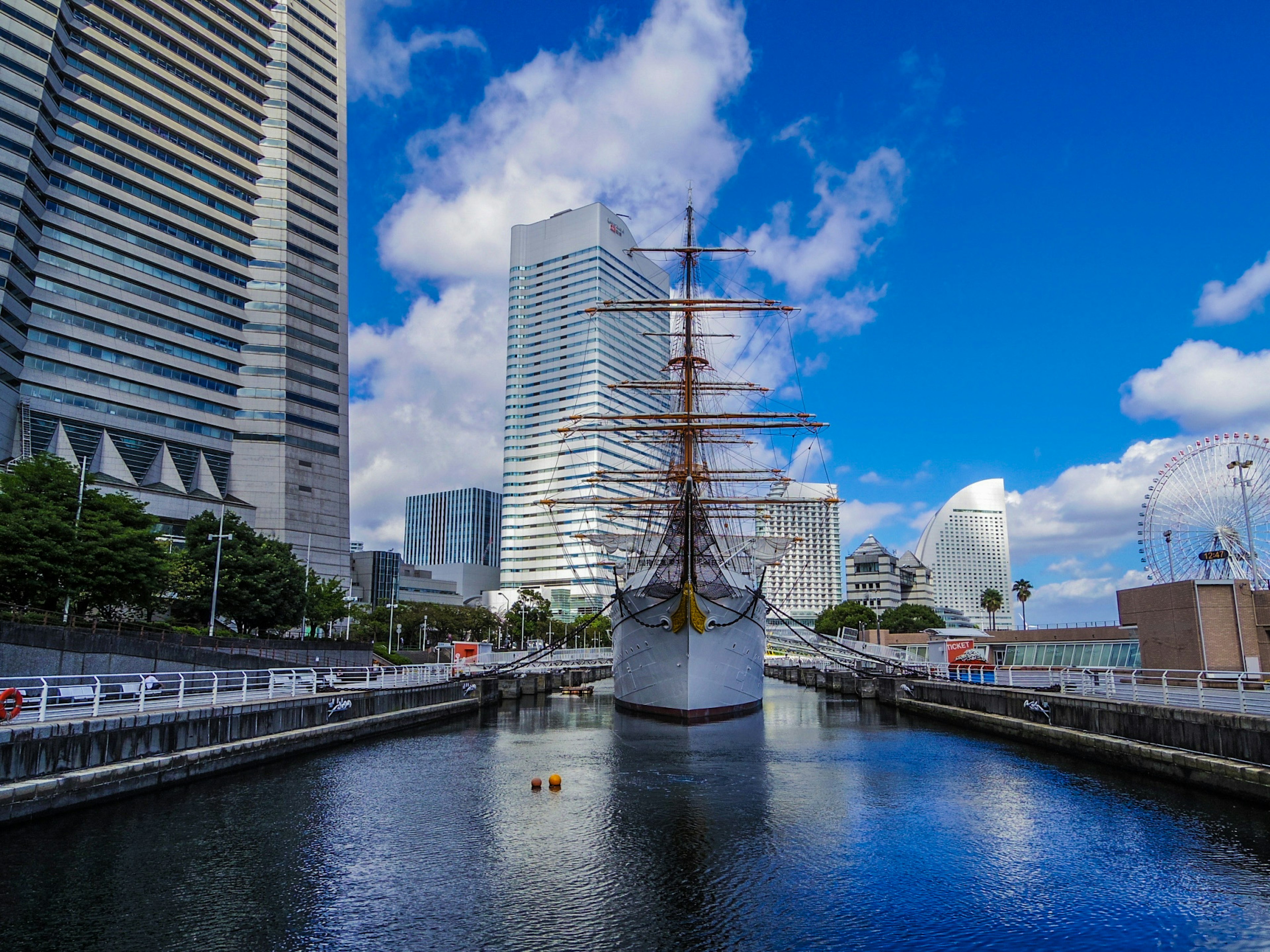 Sailing ship docked in a harbor surrounded by skyscrapers and blue sky