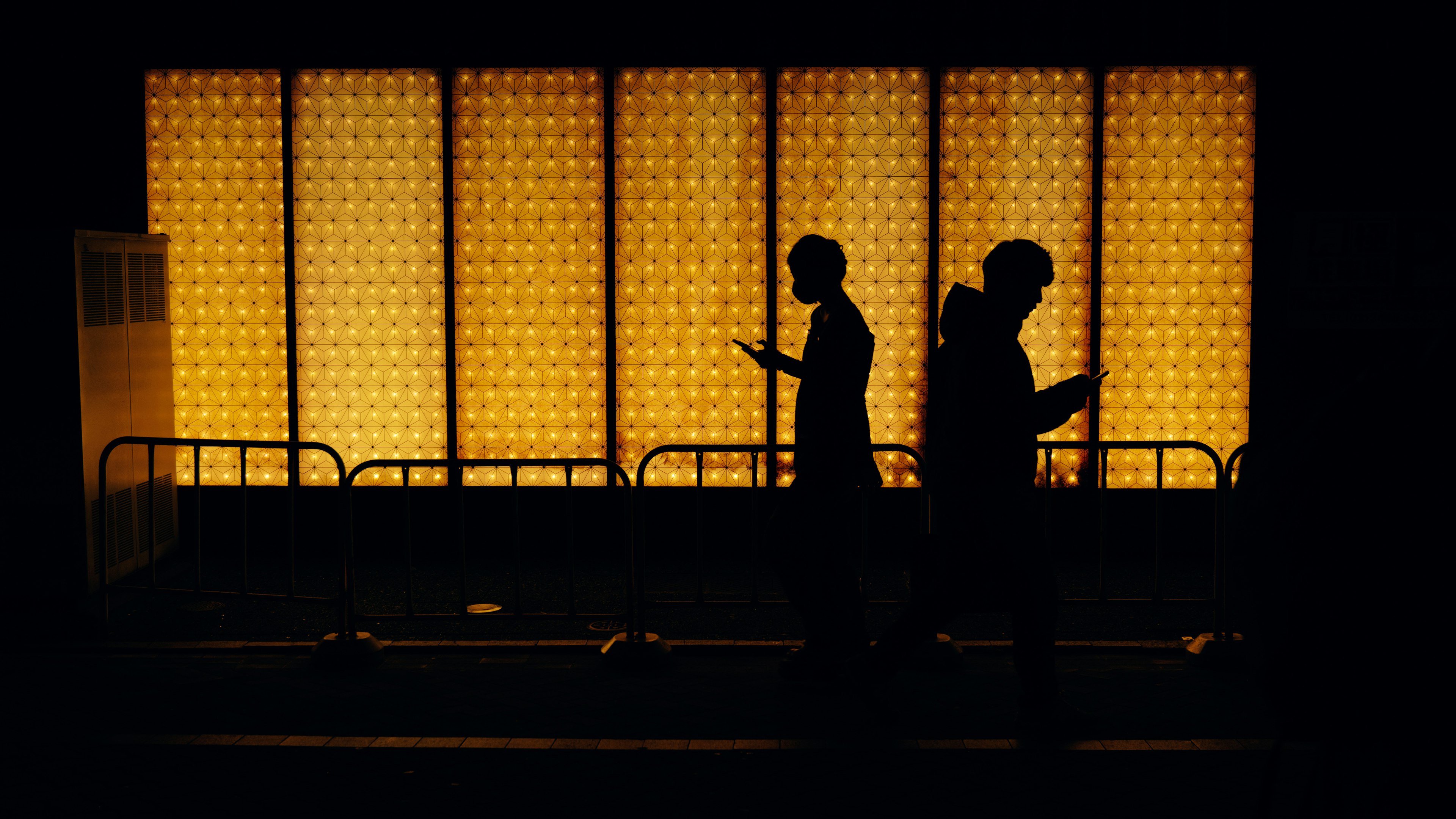 Silhouetten von Personen, die vor einem orange beleuchteten Hintergrund gehen