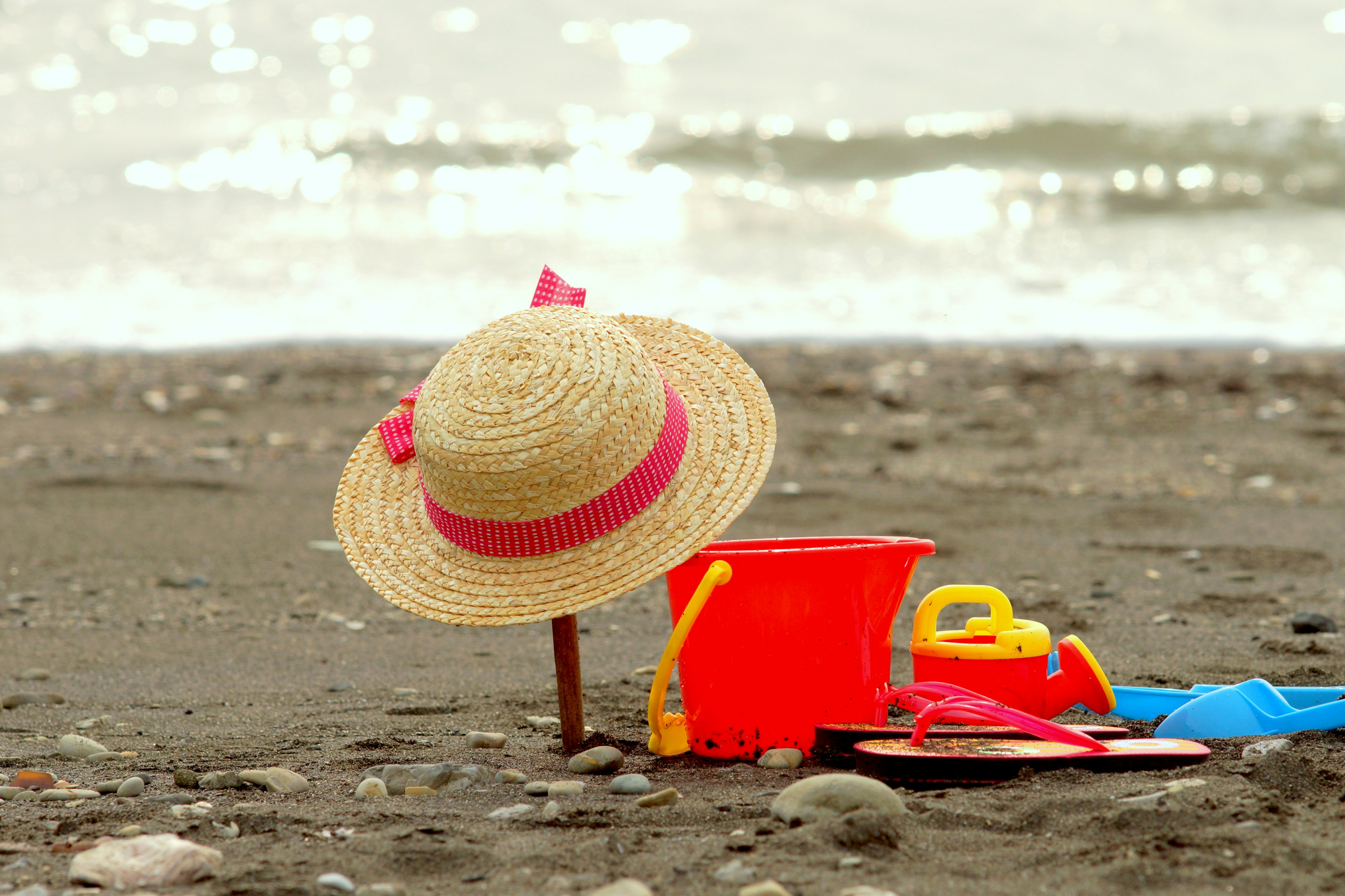 Chapeau en paille et seau de jouet sur le sable de la plage