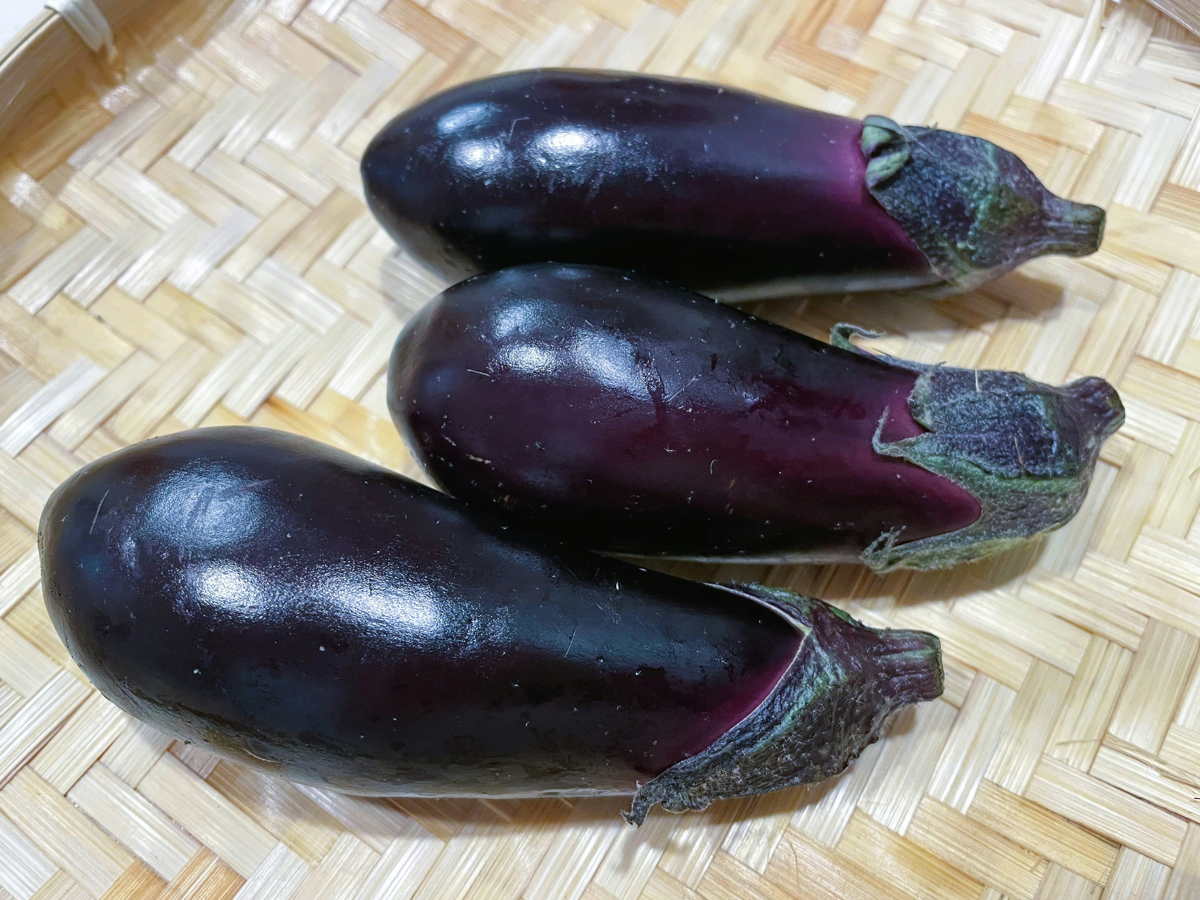 Three eggplants in dark purple resting on a woven bamboo basket