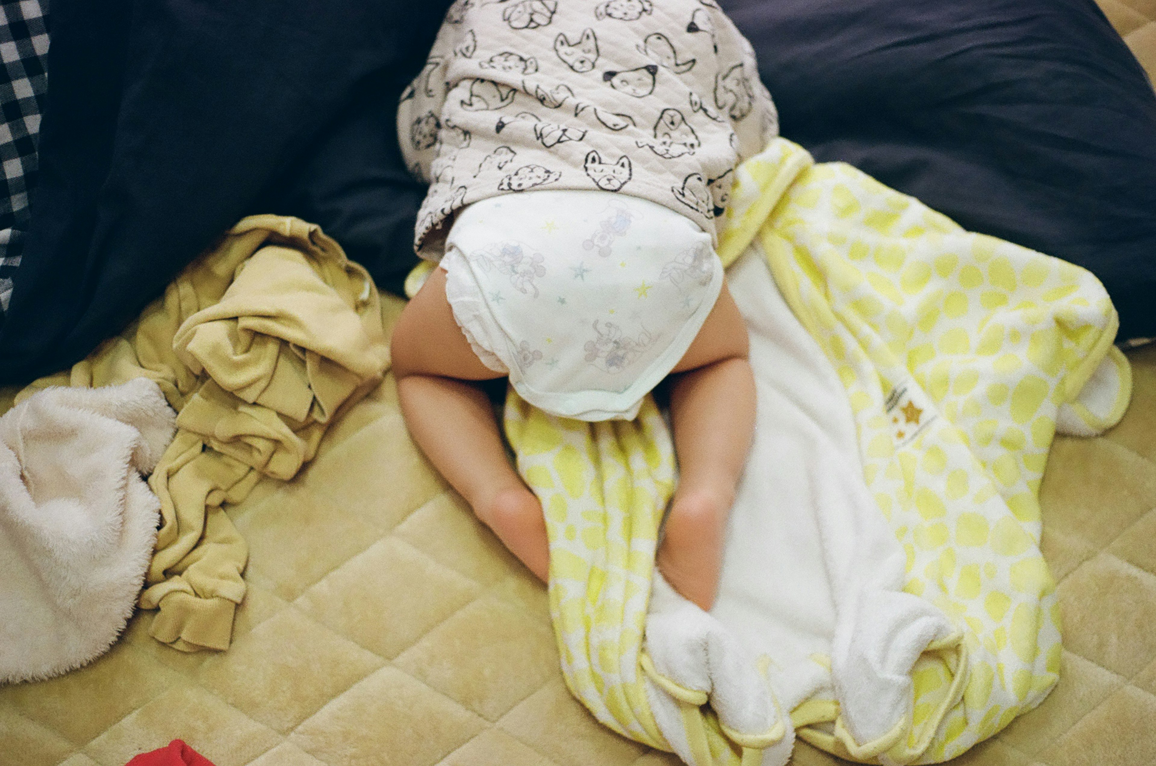 Seorang bayi terbaring tengkurap di atas selimut kuning