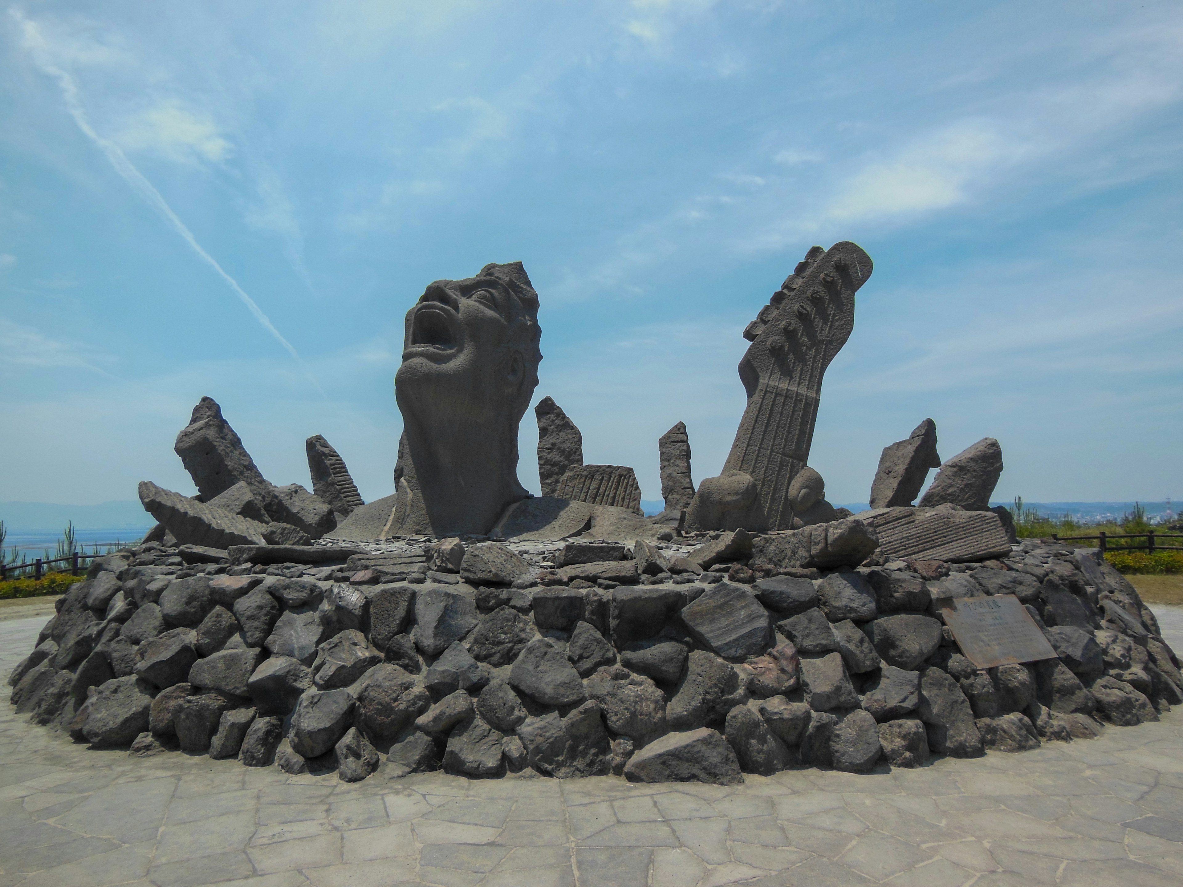 A stone sculpture depicting a figure screaming towards the sky surrounded by rocks