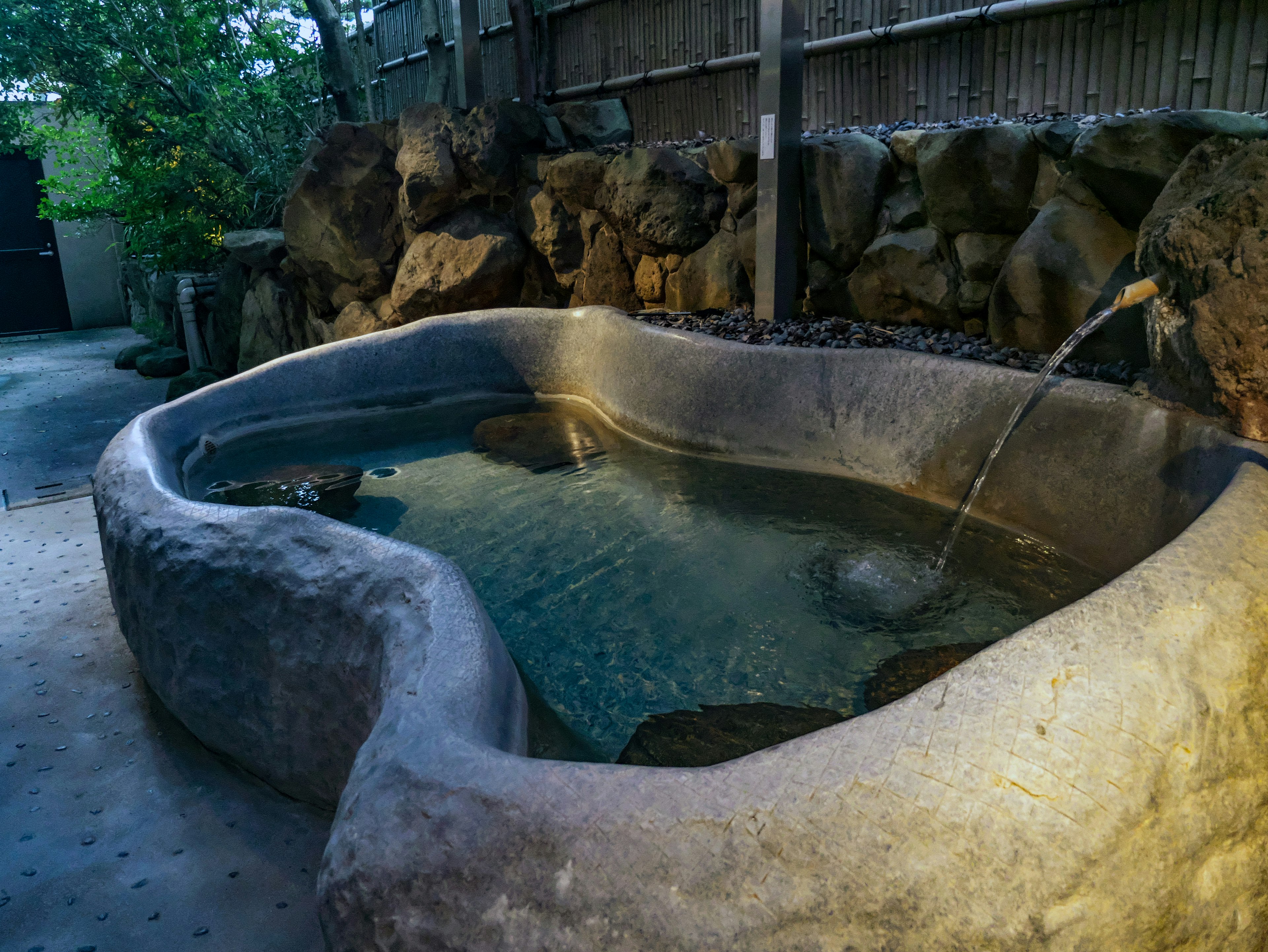 Natural stone hot tub with flowing water surrounded by greenery