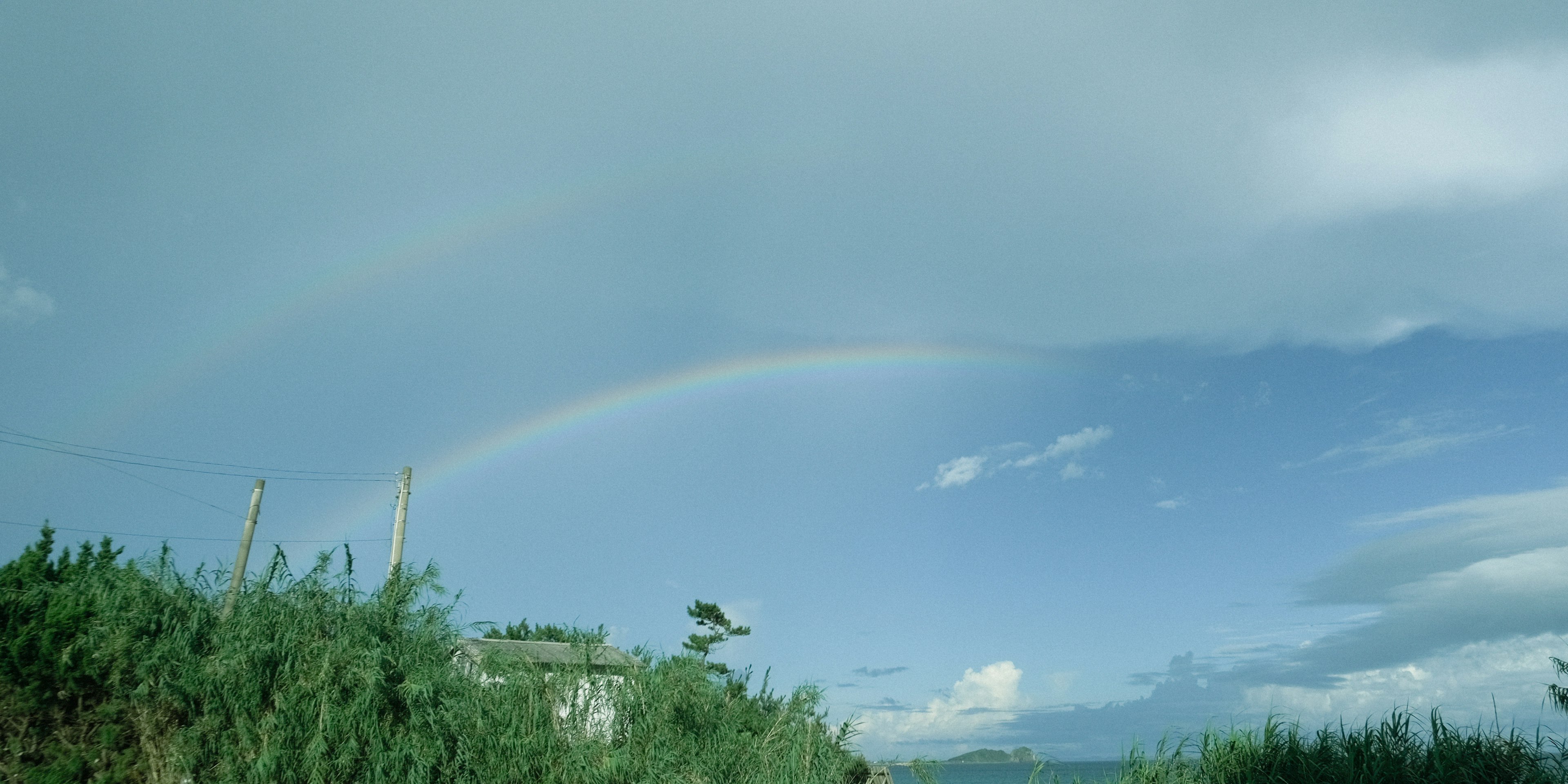 Un arc-en-ciel s'étendant dans un ciel bleu avec des nuages légers et un avant-plan herbeux