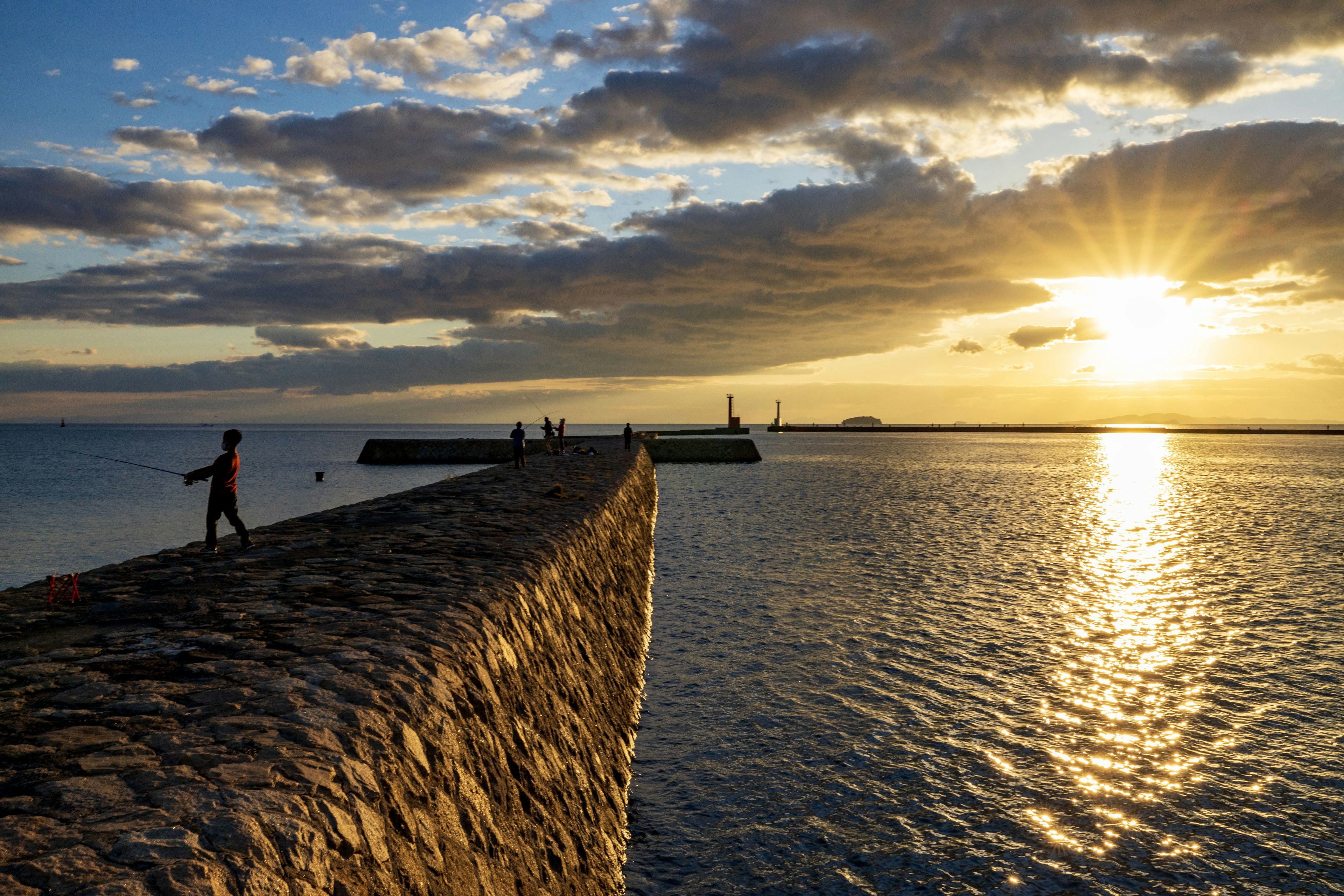 A person walking on a stone pier with a beautiful sunset in the background