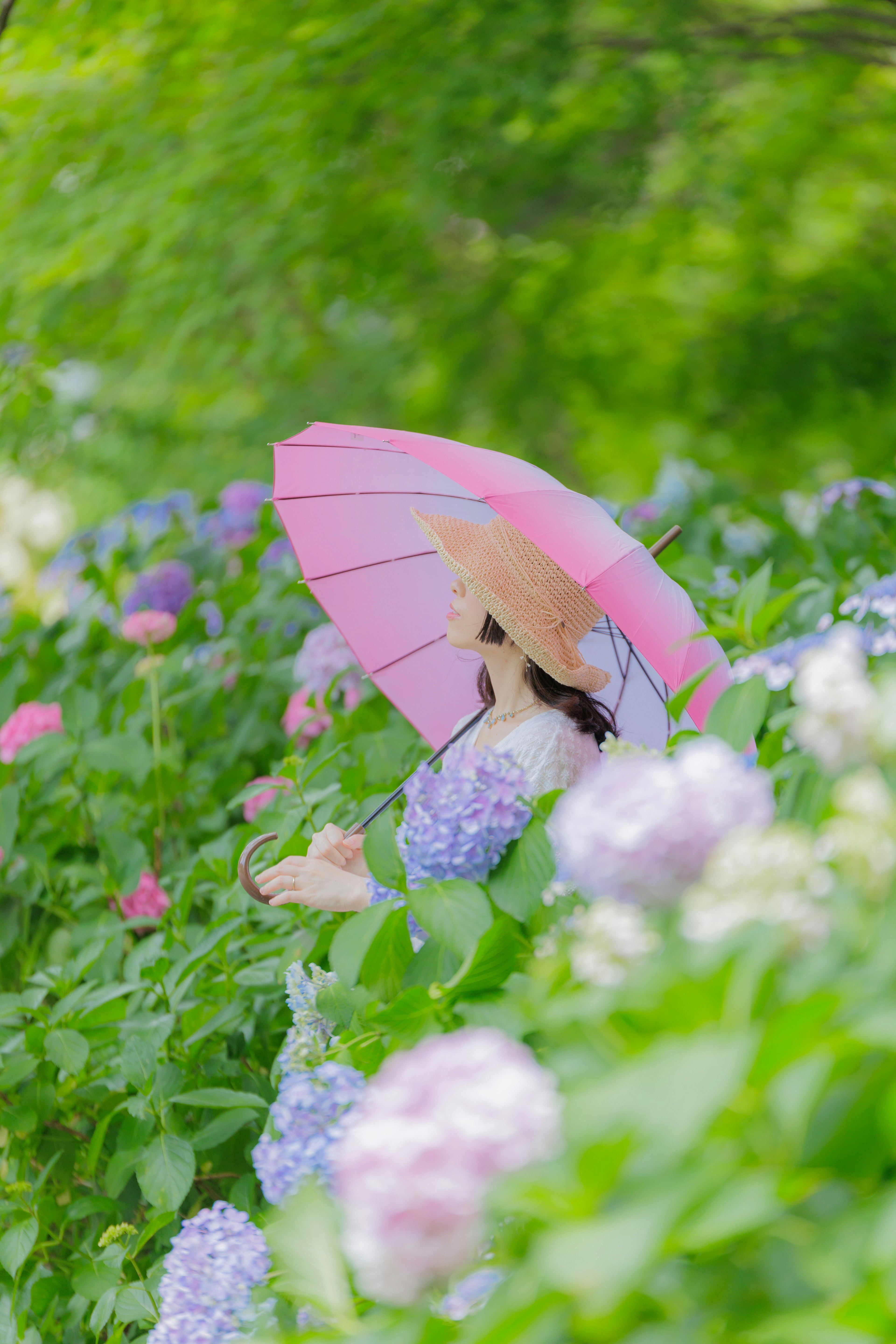 Donna con un ombrello rosa circondata da fiori di ortensia