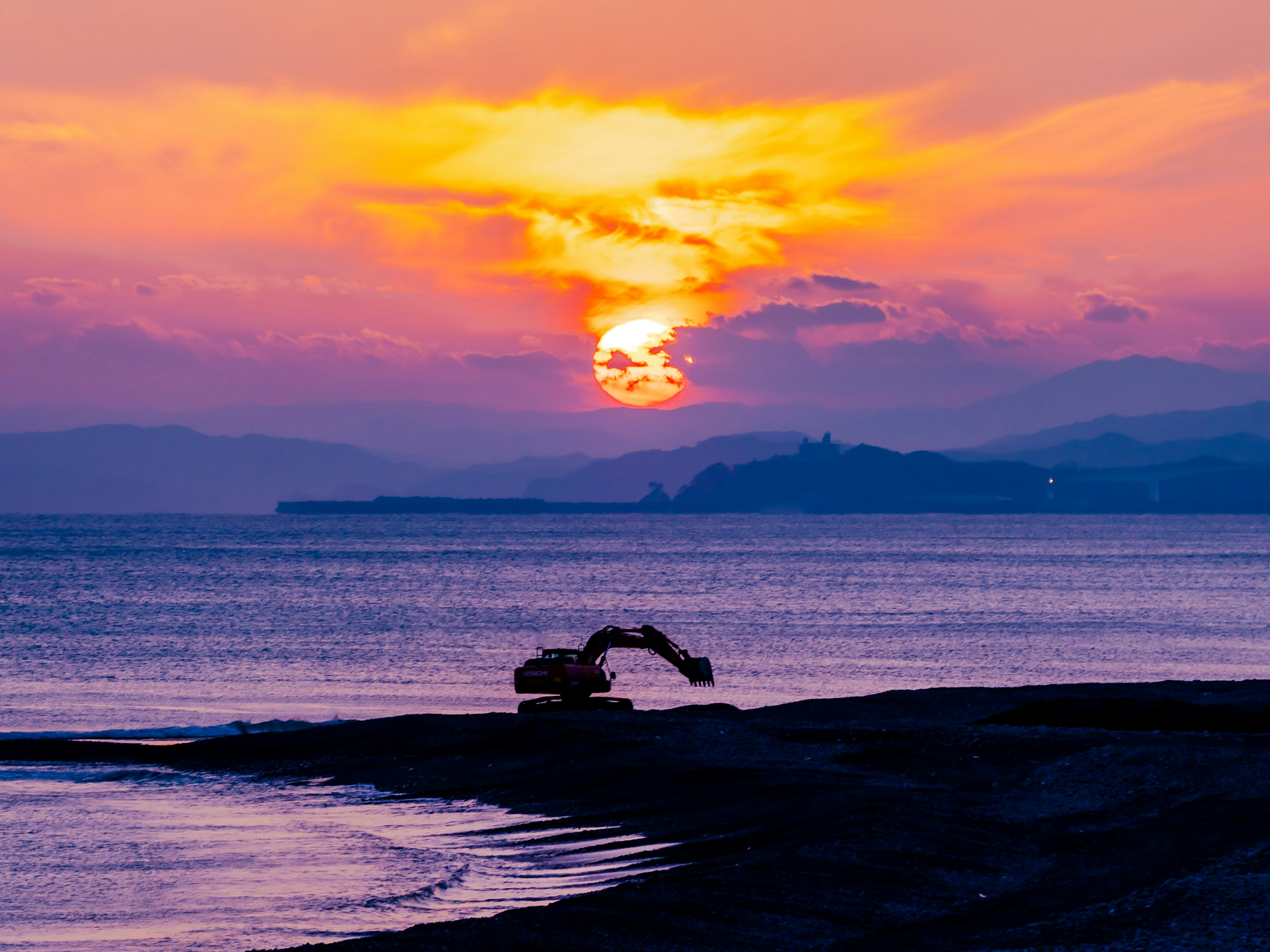 夕日が海に沈む美しい景色と海岸で作業する重機