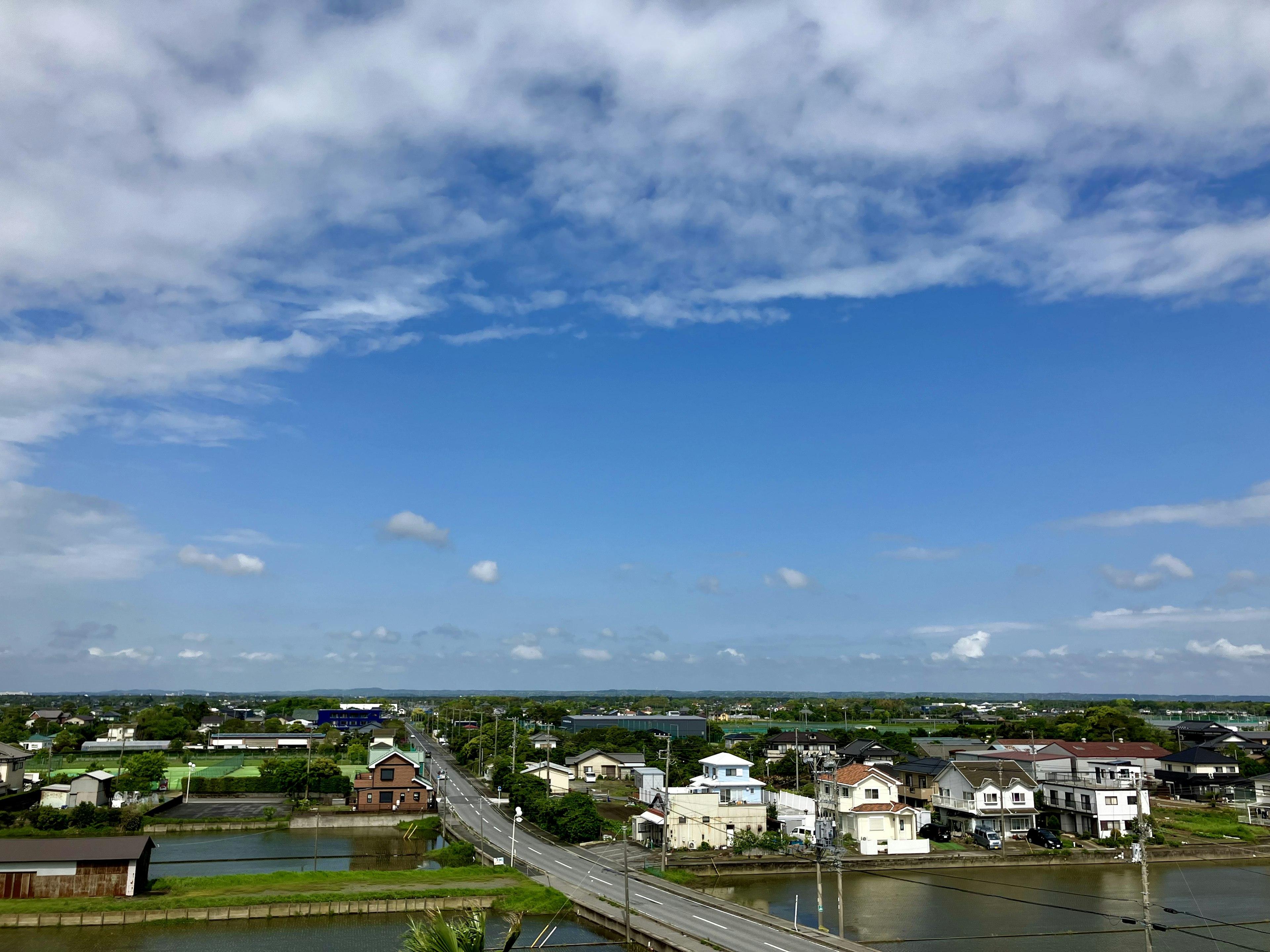 青い空と白い雲が広がる風景 田園地帯に点在する家々と橋が見える