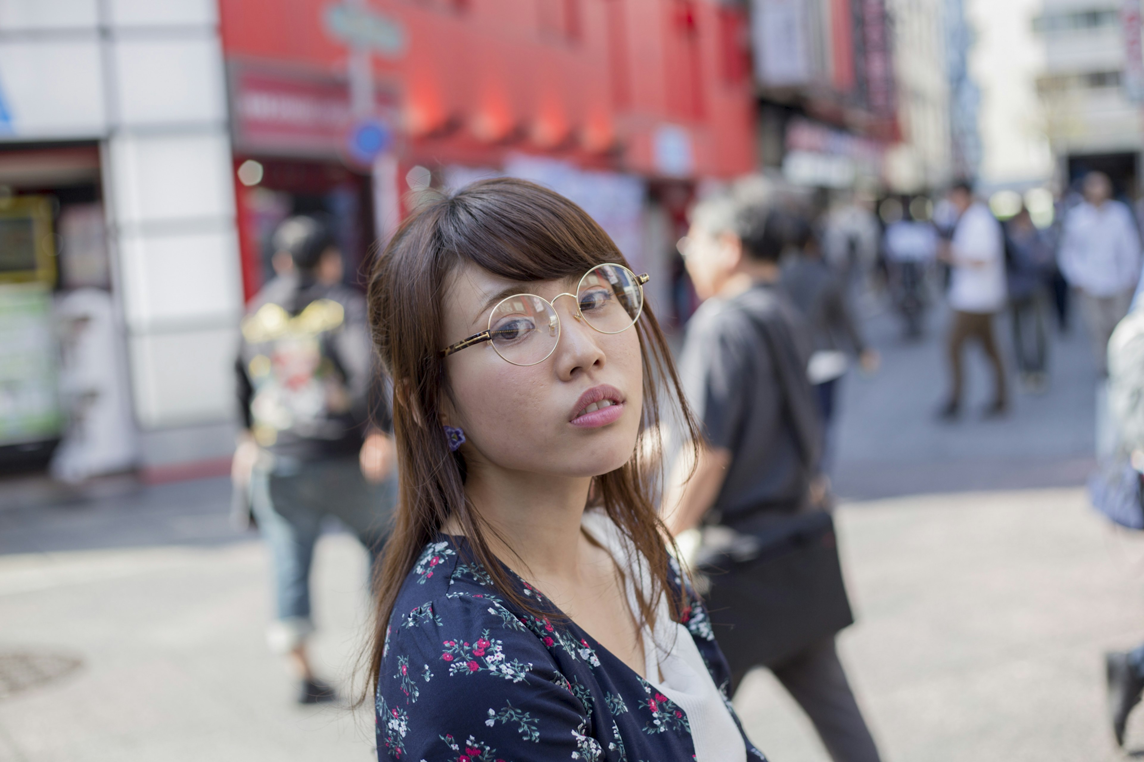 Frau mit Brille, die die Kamera vor einem roten Gebäude ansieht