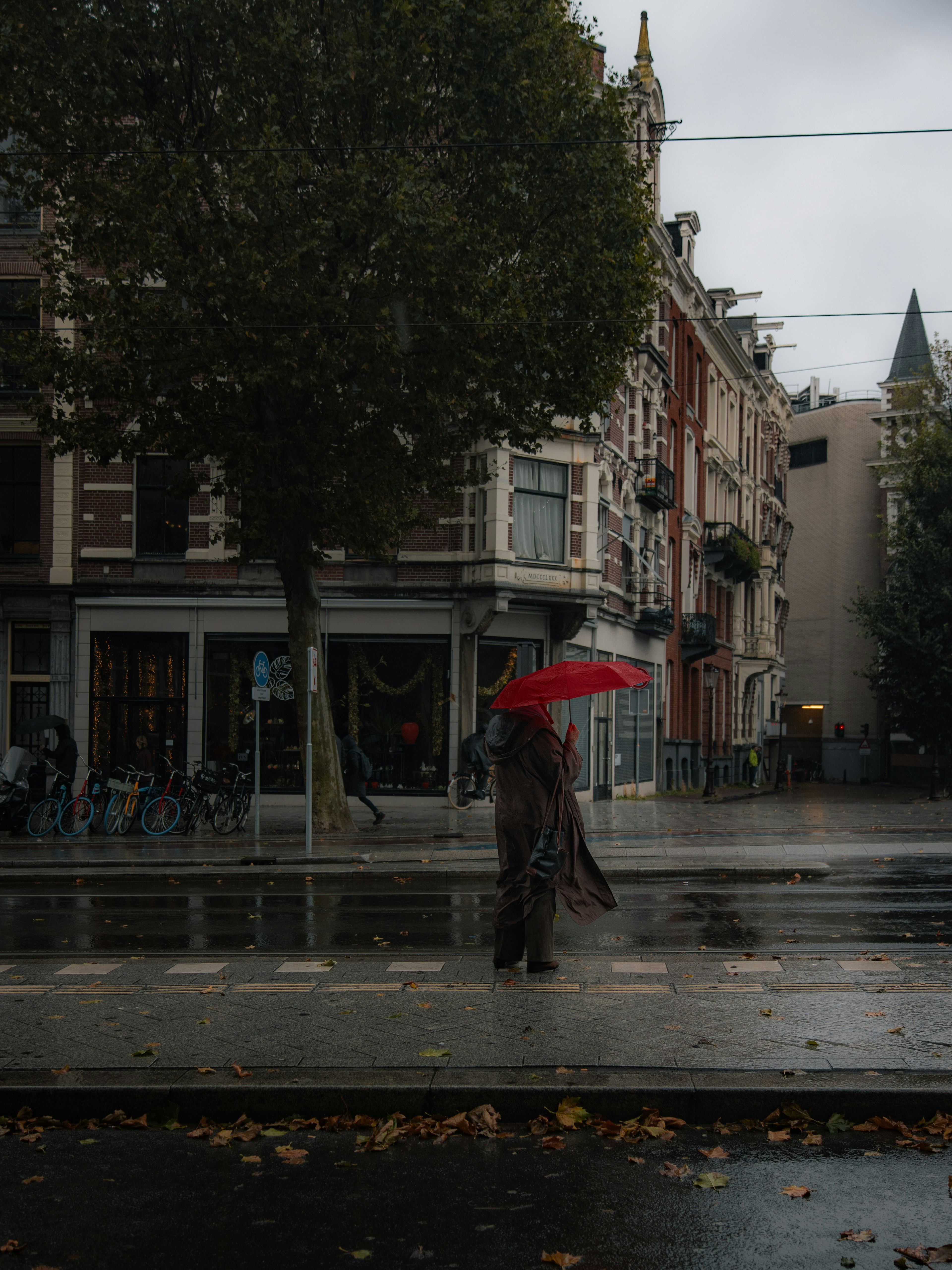 赤い傘を持った人物が雨の中を歩いている街の風景