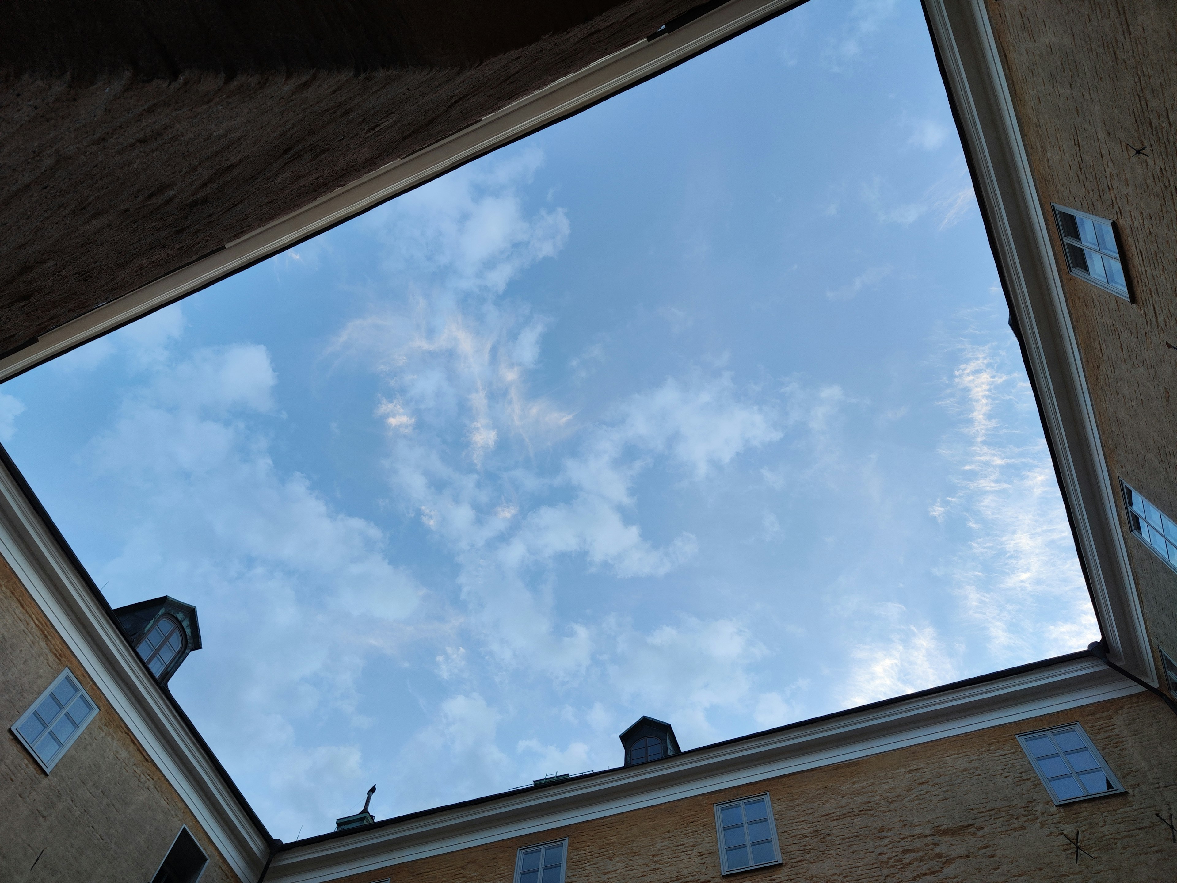 Interior view of a building with a square opening showing the blue sky and clouds