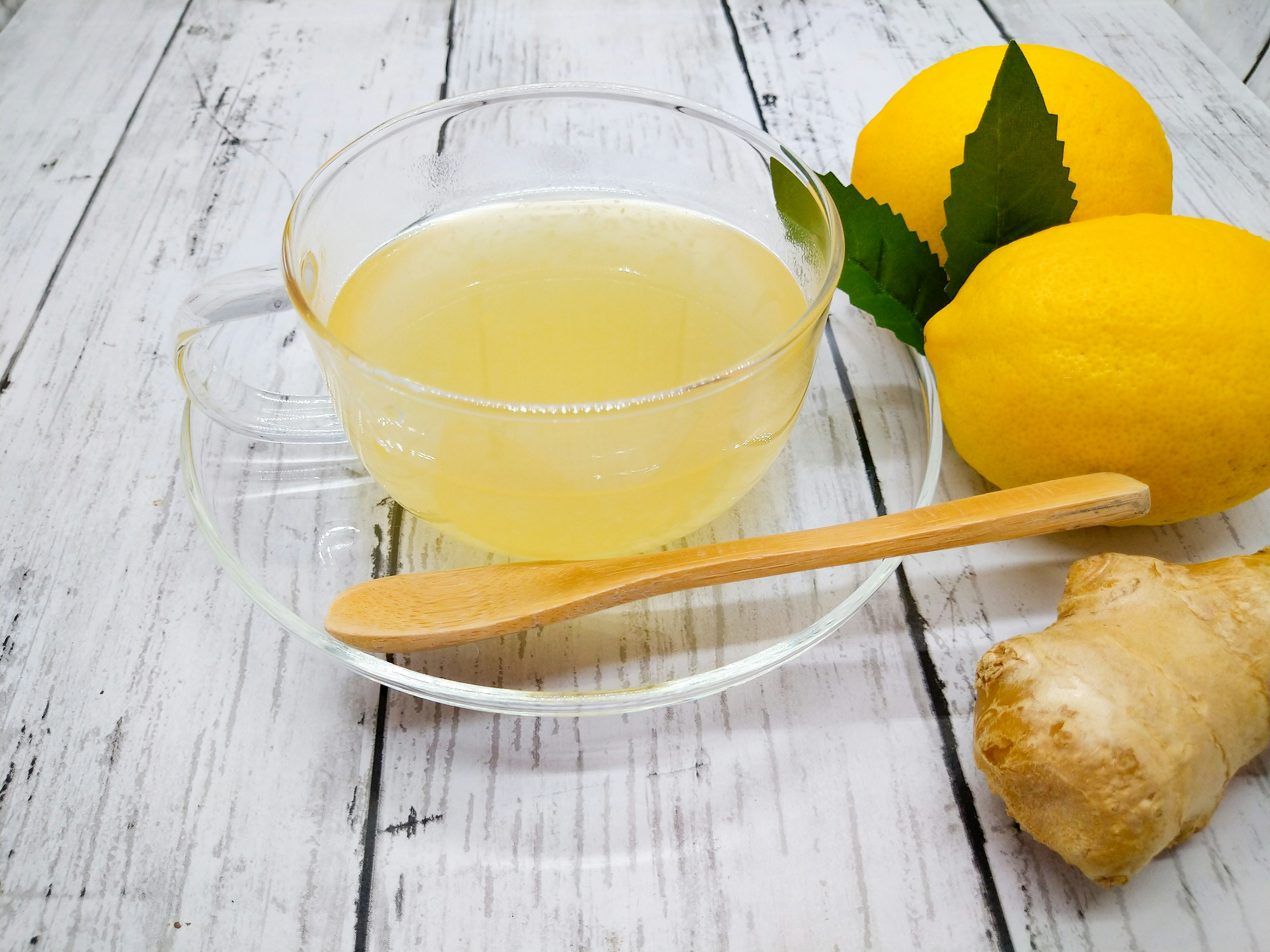 Clear cup with lemon ginger tea alongside yellow lemons and ginger root